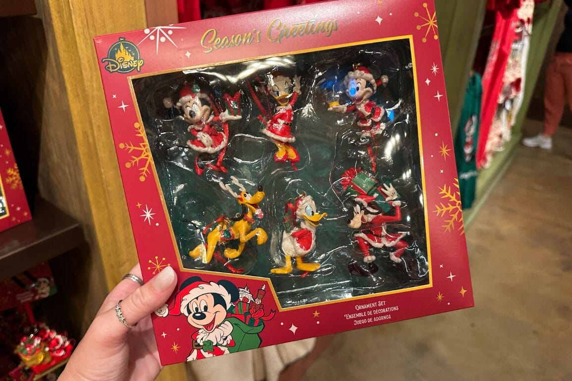 دستی که ست محصولات تعطیلات دیزنی ورلد را با حضور میکی، مینی، دونالد، دیزی، گوفی و پلوتو در لباس‌های جشن پارک نگه داشته است—قلعه‌ای دیده نمی‌شود.