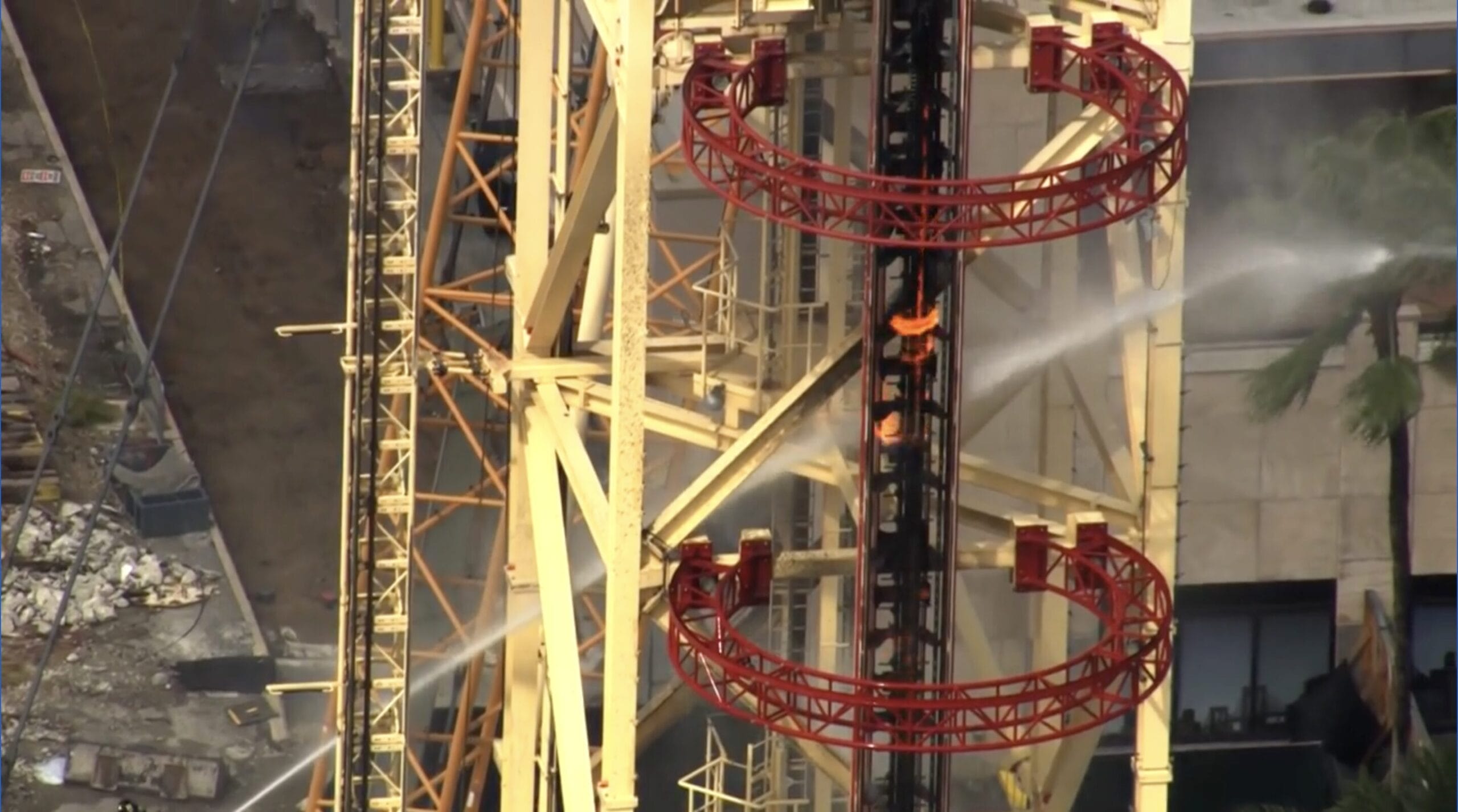 Firefighters spray water on two workers atop a construction crane, an intense rescue scene reminiscent of park show spectacles, no castles.