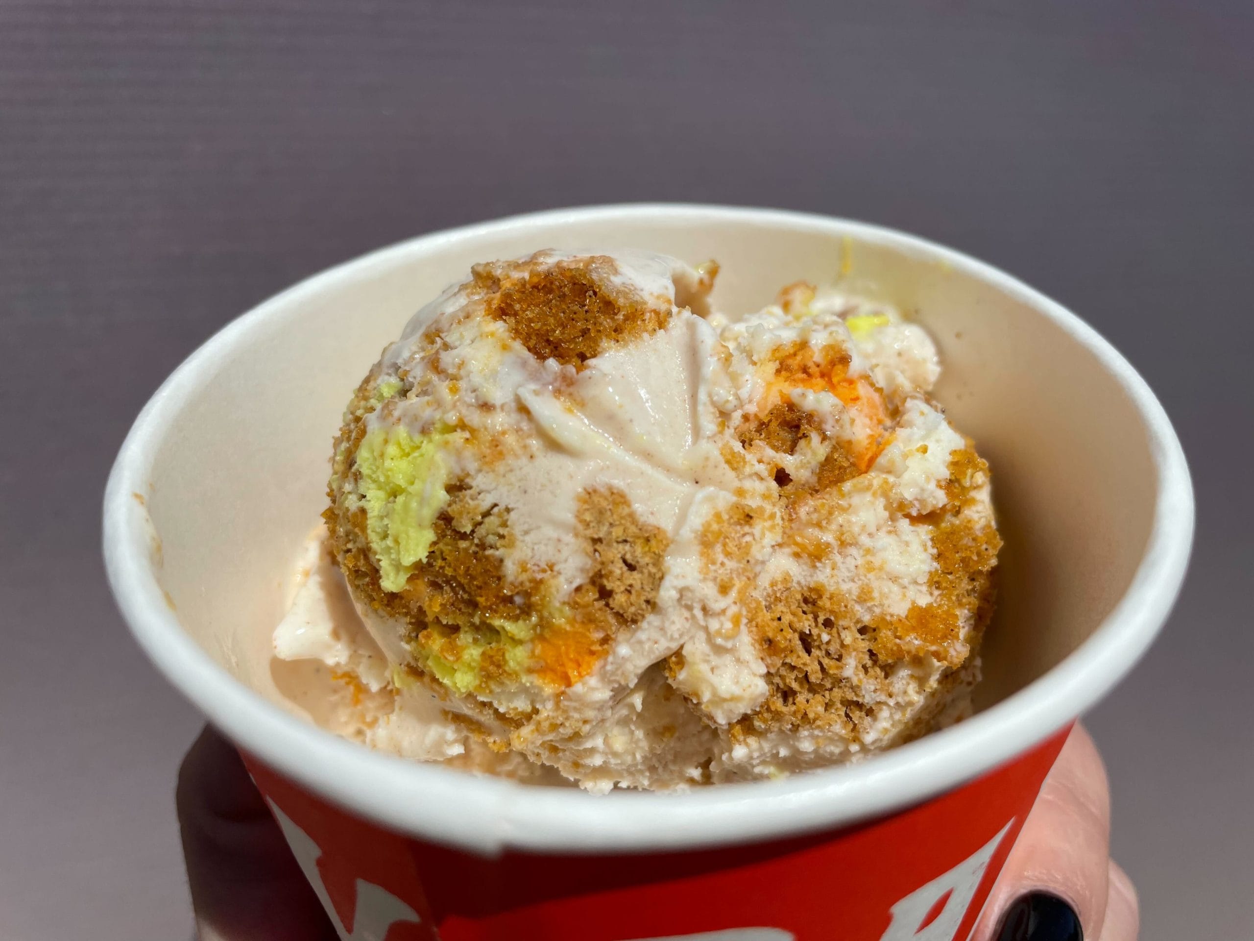 A hand holds a Salt & Straw cup with a scoop of Jack o' Lantern pumpkin bread ice cream with a cream cheese frosting swirl.
