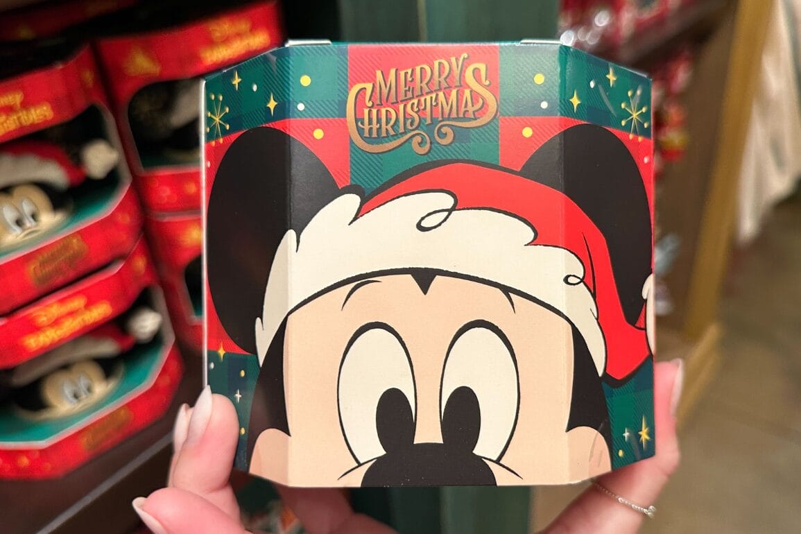 دستی که محصولات تعطیلات دیزنی ورلد را با طرح میکی ماوس در کلاه سانتا و متن «کریسمس مبارک» نگه داشته است، نمادی از جشن‌های پارک.