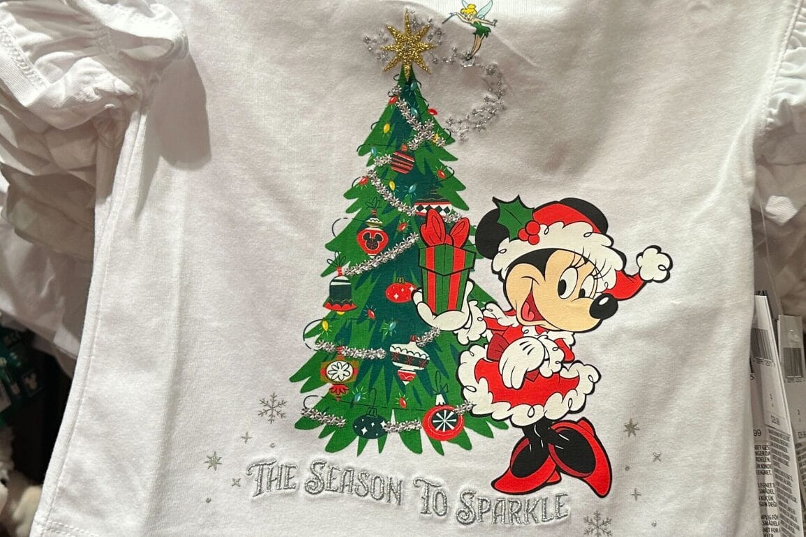 تی‌شرت سفید با طرح مینی ماوس در لباس سانتا کنار یک درخت—عالی برای سفر به پارک دیزنی و گرفتن عکس‌های خاطره‌انگیز با قلعه در ایام جشن.