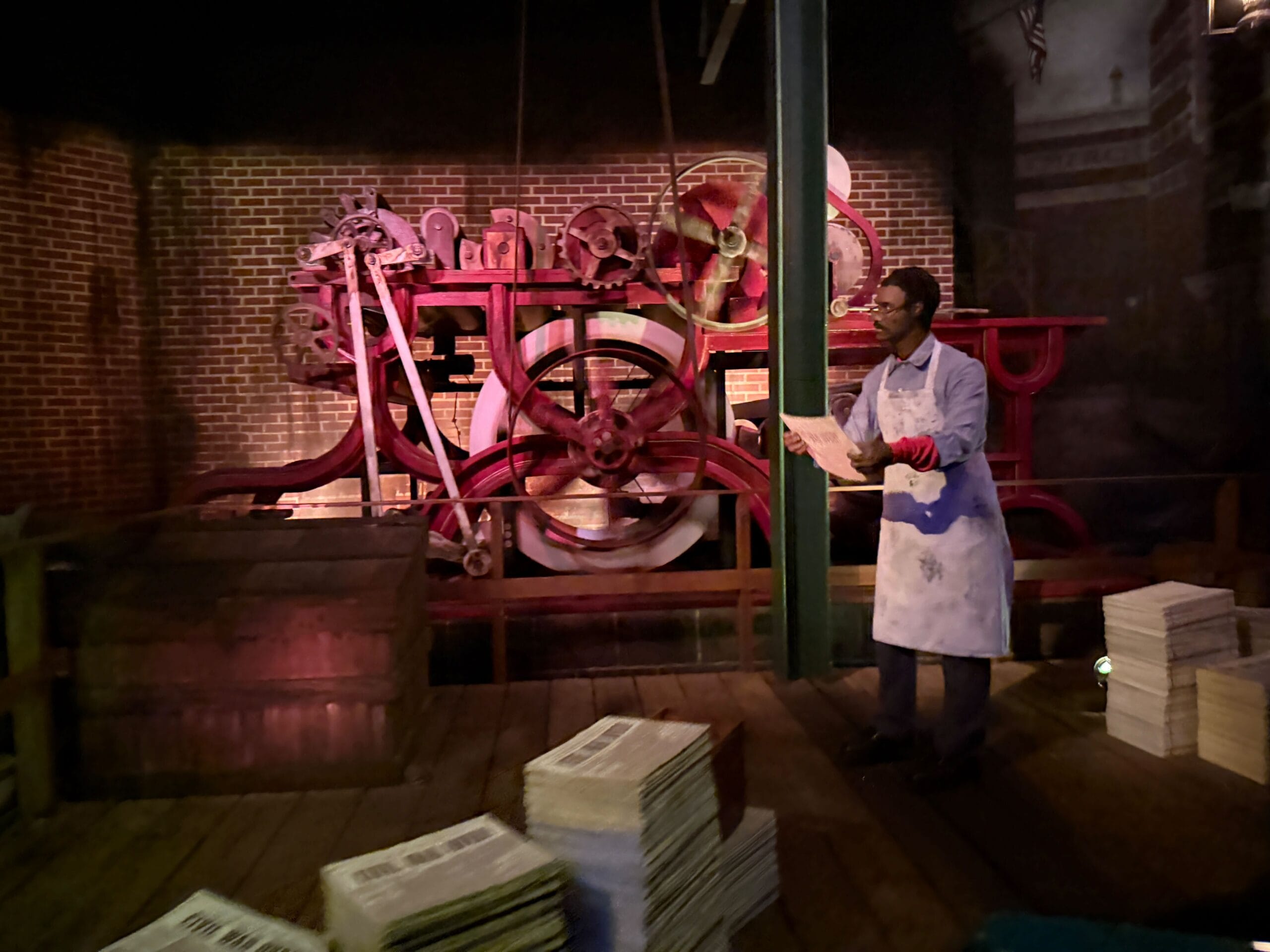 A man in an apron stands by newspapers and red machinery as a reimagined Main Street shop reopens after Disney-style refurbishment.