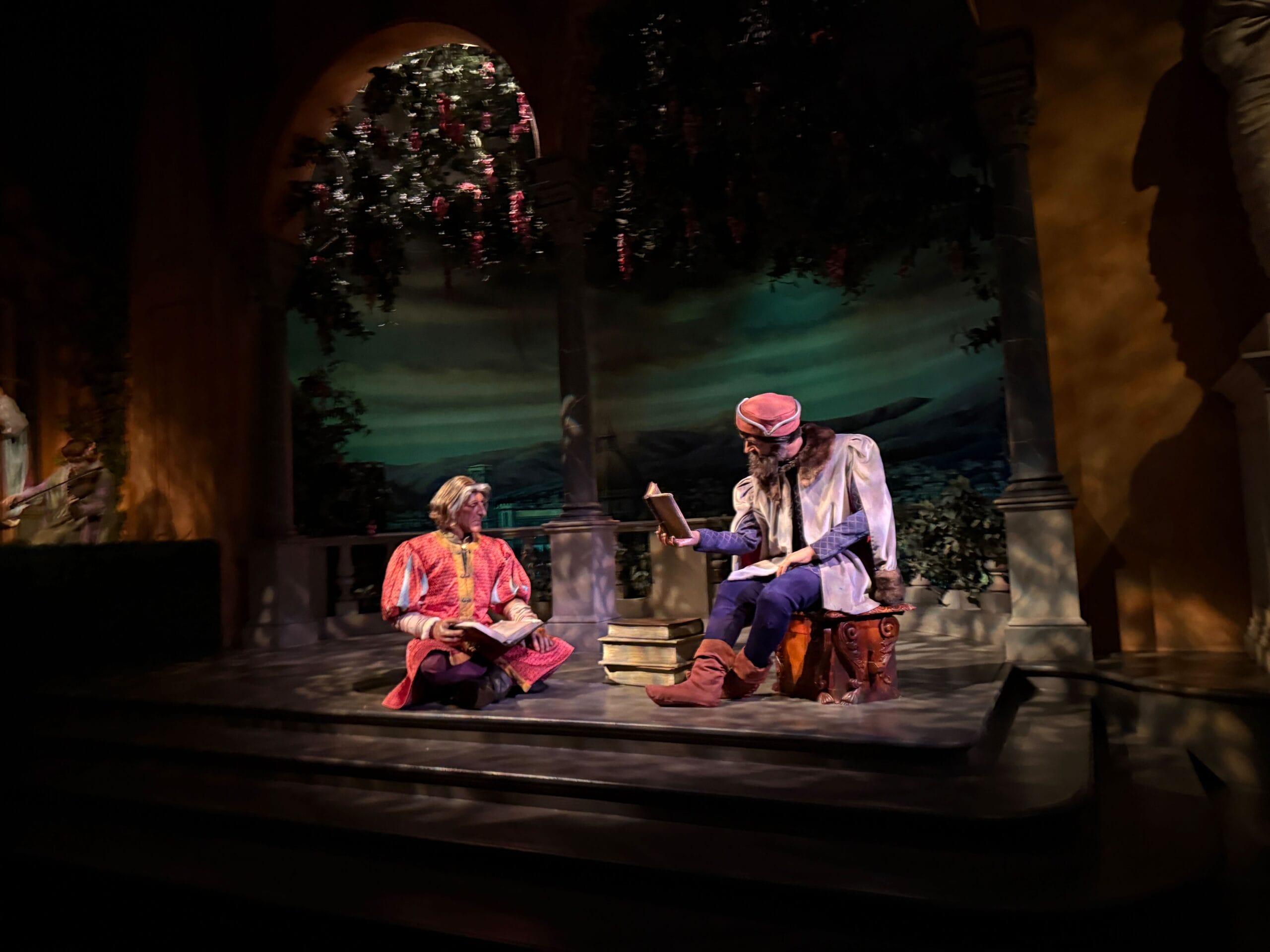 Two figures in Renaissance attire read under lush arches, reminiscent of Epcot’s World Showcase near Spaceship Earth at Disney Parks.