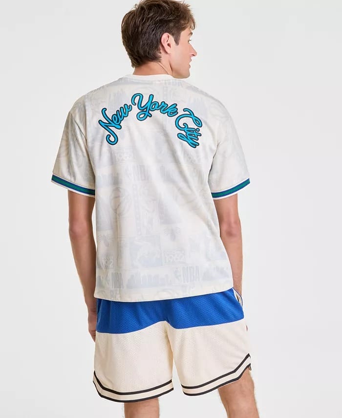 A man in a white "New York City" shirt and NBA-style white shorts with blue and black trim stands at a Disney park.