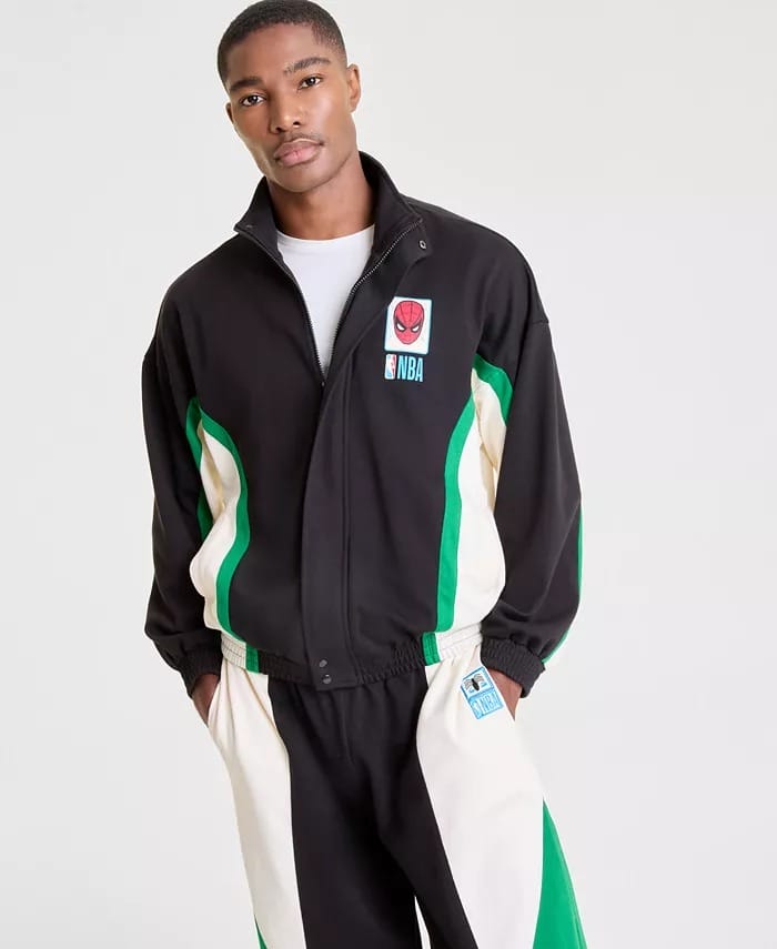 Man in a black, white, and green NBA tracksuit, hands in pockets, against a plain backdrop—not reminiscent of any Disney castle.