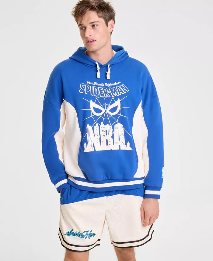 A young man in a blue Spider-Man NBA hoodie from Macy's and white basketball shorts stands against a simple backdrop, not in a Disney park.