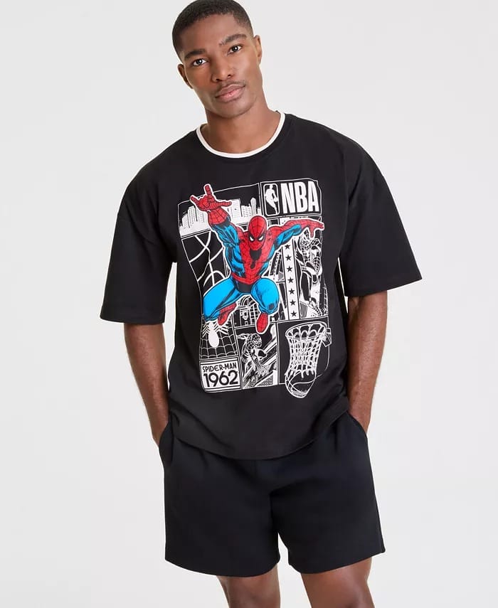 A man in a Macy's Collection black T-shirt with a Spider-Man and NBA graphic stands hands-in-pockets, as seen at Disneyland.