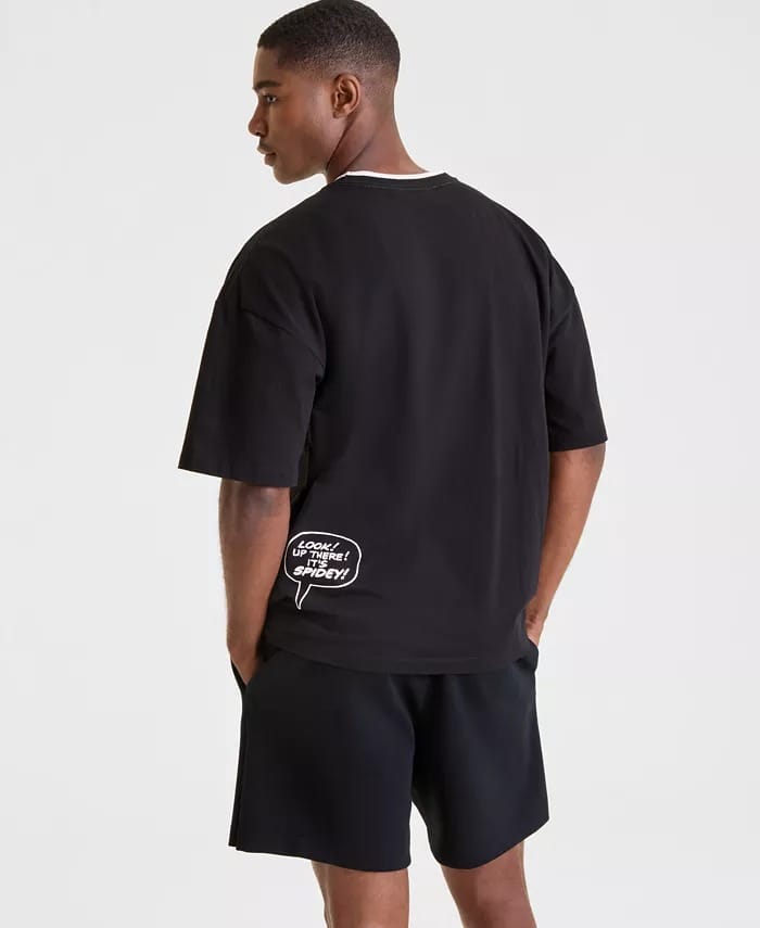 A man in a black Macy's Collection T-shirt and shorts stands with hands in pockets at a Disney park, castle not visible nearby.