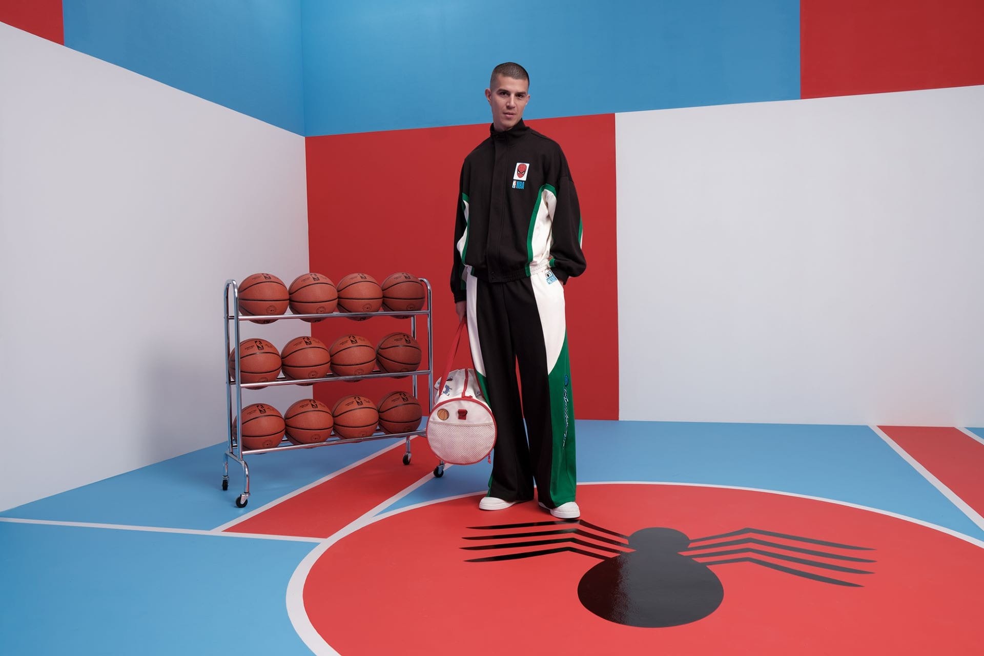 A person in a Macy's Collection tracksuit stands on a Spider-Man logo court, holding a basketball bag, not near any Disney castle.