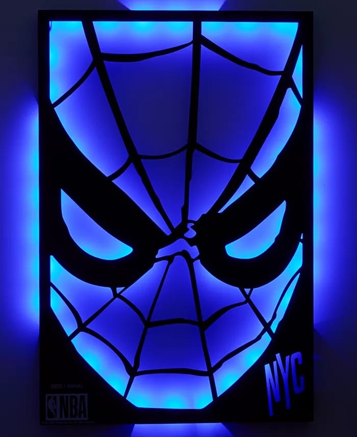 A glowing blue neon Spider-Man mask sign with "NYC," NBA logos, and Macy's Collection text, echoing the vibrant style seen in Disney gift shops.