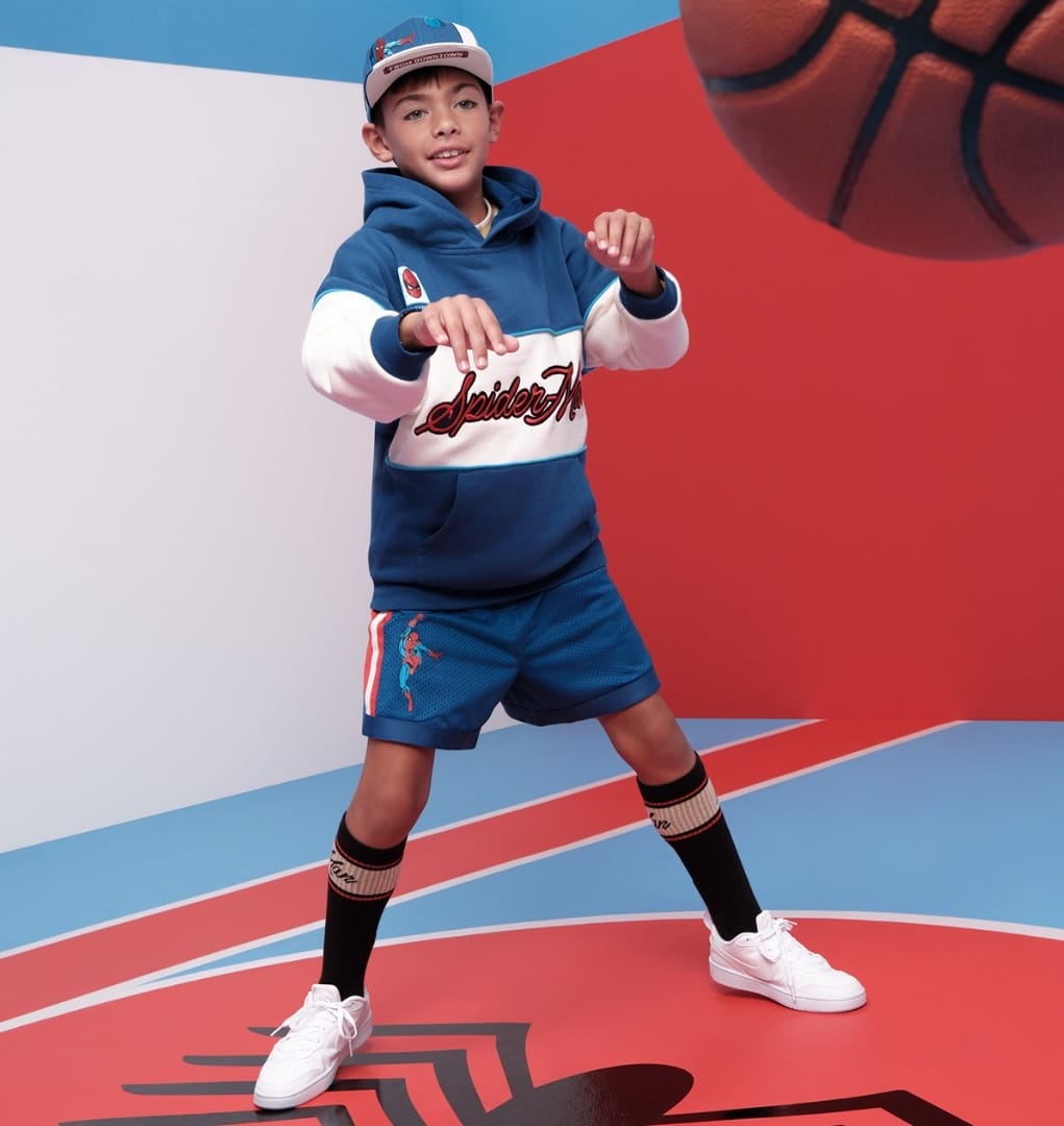 Boy in a sporty blue NBA outfit poses on a colorful court, basketball in the air above him—no Disney castle visible to compare.