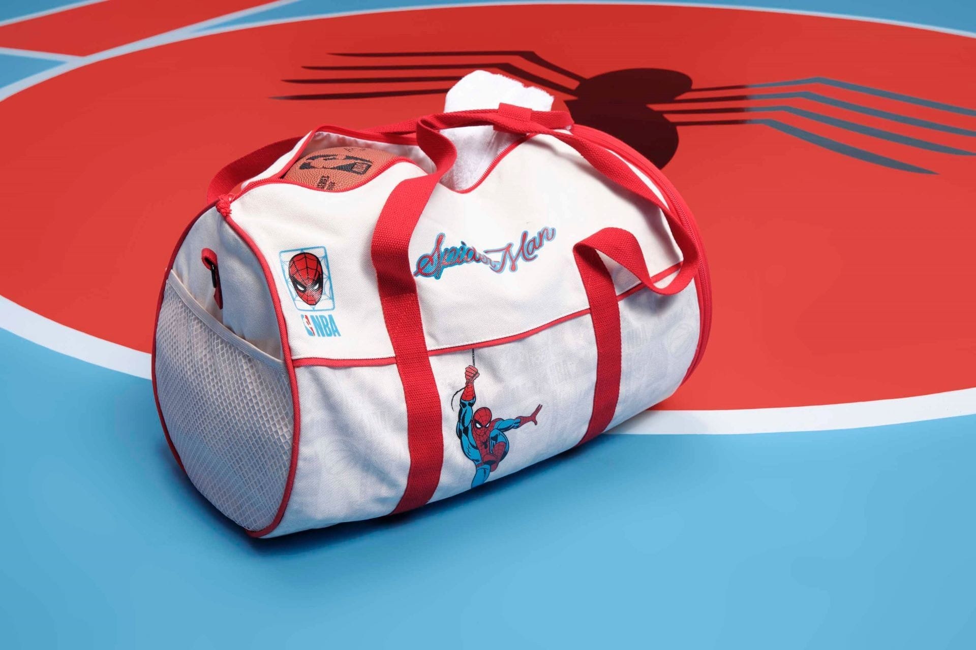 A white and red Macy's duffle bag with Spider-Man graphics rests on a blue and red Spider-Man logo floor, similar to Marvel areas in Disney parks.