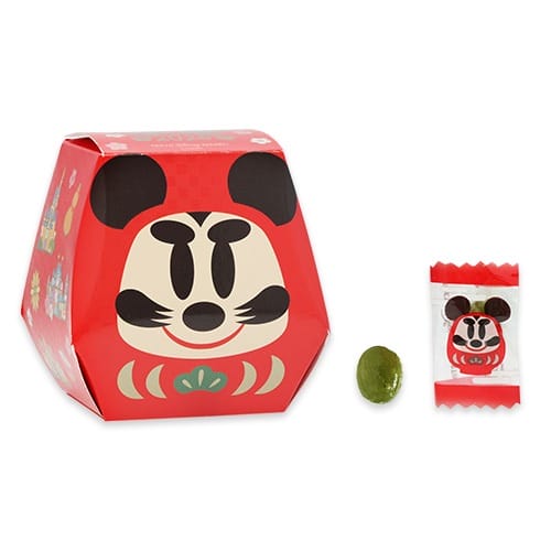A red hexagonal box with a cartoon face from Tokyo Disney Resort’s 2026 New Year line sits next to green candy, no castle visible.