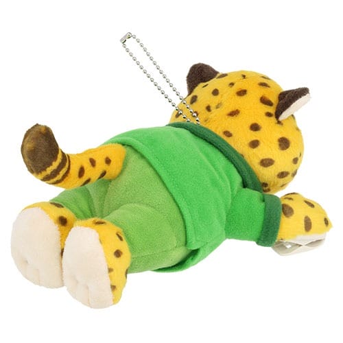 Plush Zootopia 2 leopard in green outfit, lying on stomach with keychain, sold at Disney parks near iconic castle backdrops.