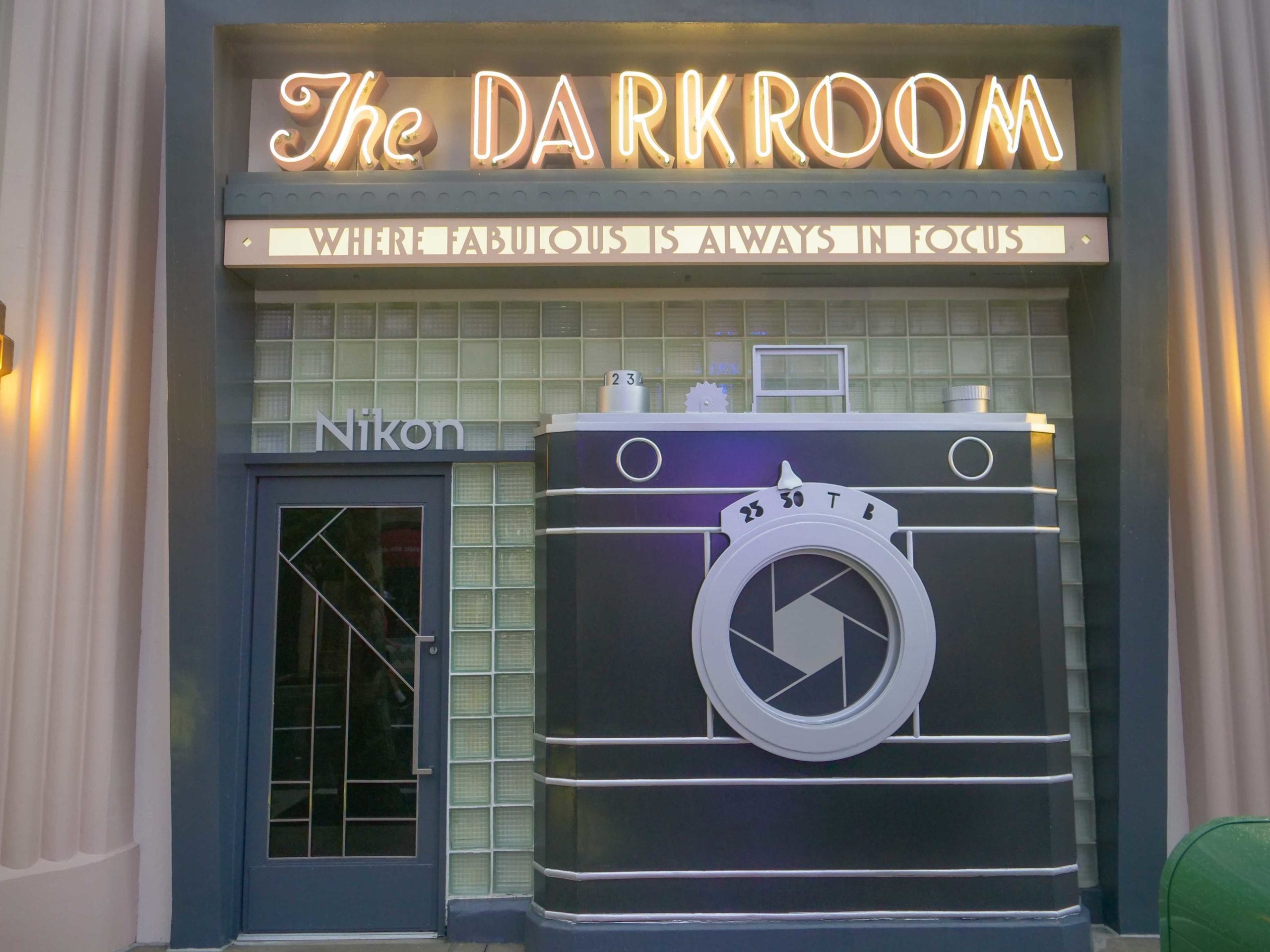 Storefront resembles a vintage camera with "The Darkroom" sign, featuring Princess Pins and Disney flair—similar to Main Street theming.