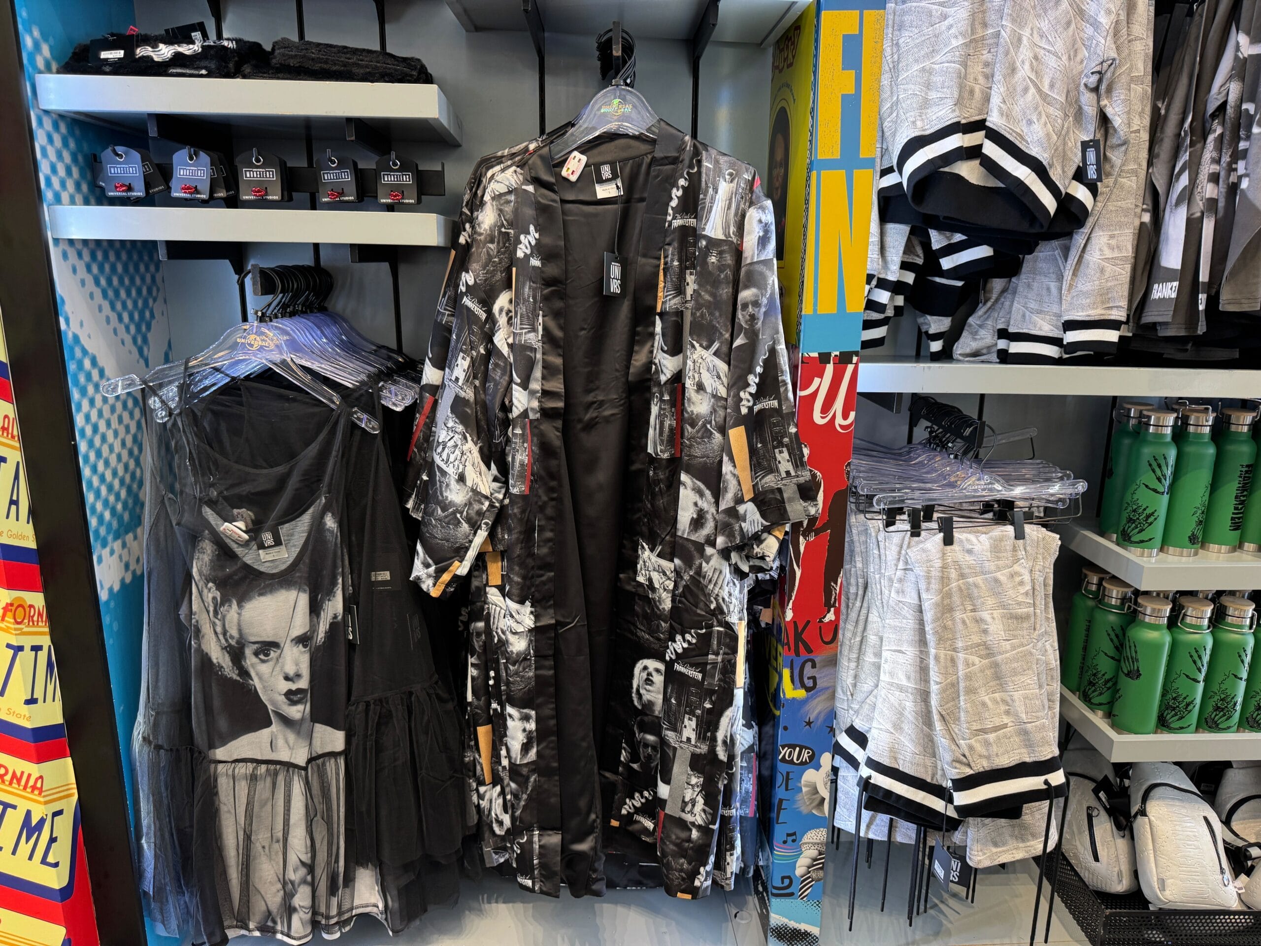 Clothing rack with Disney-style black-and-white graphic shirts, shorts, green water bottles, and a dress inspired by art icons.