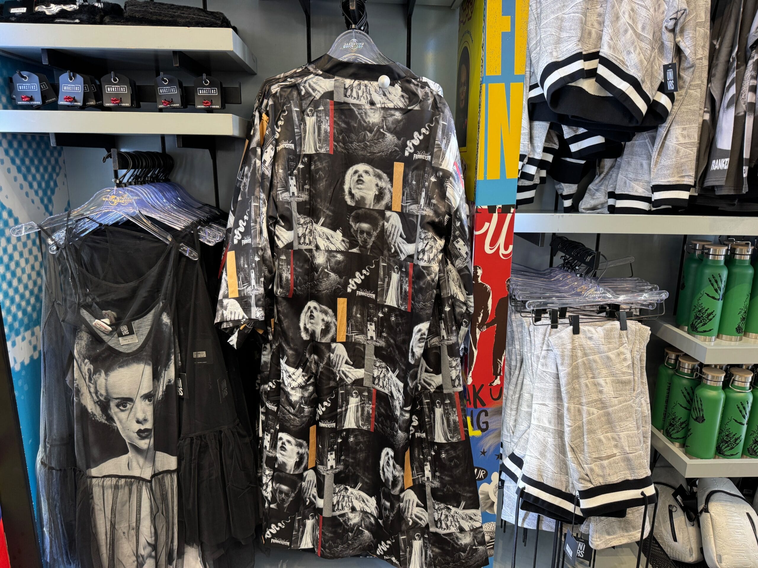 Clothing display with black-and-white horror prints (reminiscent of Disney’s Haunted Mansion), shorts, shirts, and green drink bottles.