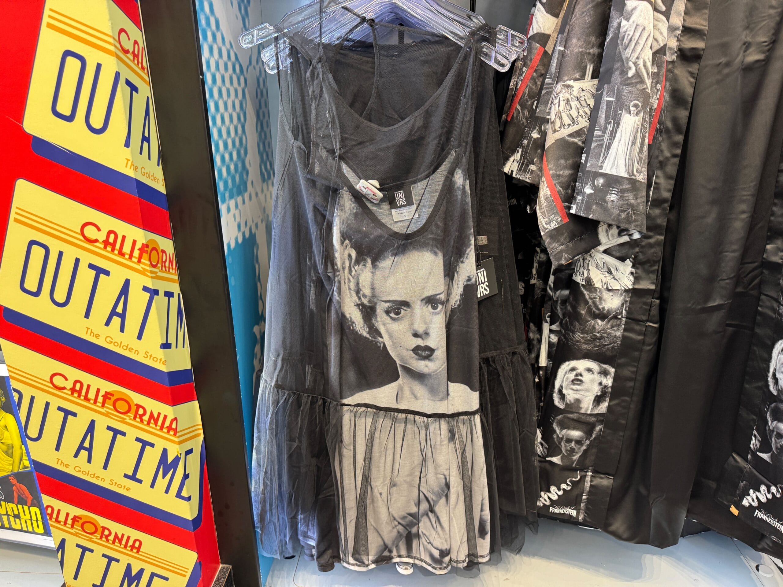 Black dress featuring a black-and-white Bride of Frankenstein print on display, next to "OUTATIME" plates—not at a Disney park.