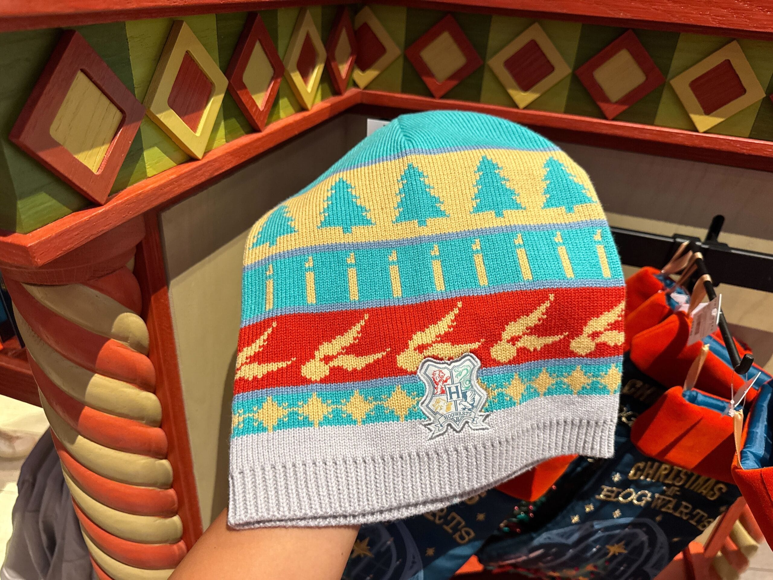 A knit beanie with trees, stars, and Hogwarts crest—perfect Harry Potter Christmas merch in a colorful store display.