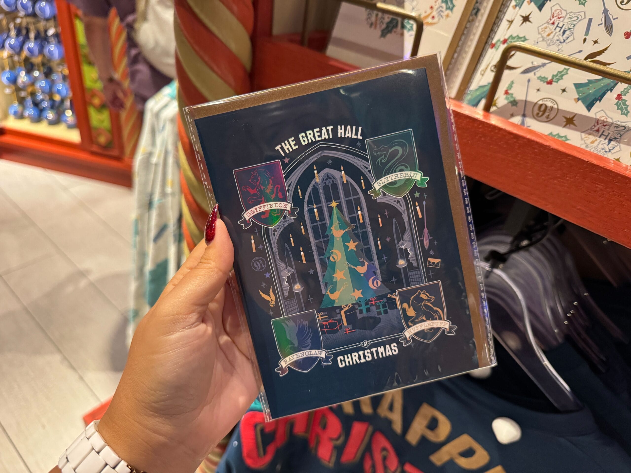 A hand holds a "Great Hall Christmas" card with Harry Potter house banners, celebrating Christmas at Hogwarts in a store.