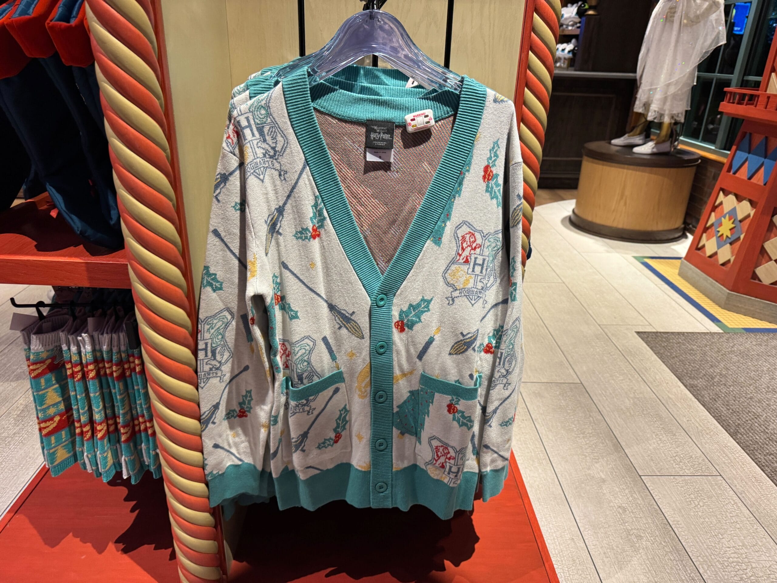 A gray and teal Harry Potter Christmas cardigan with festive designs hangs on a store rack.