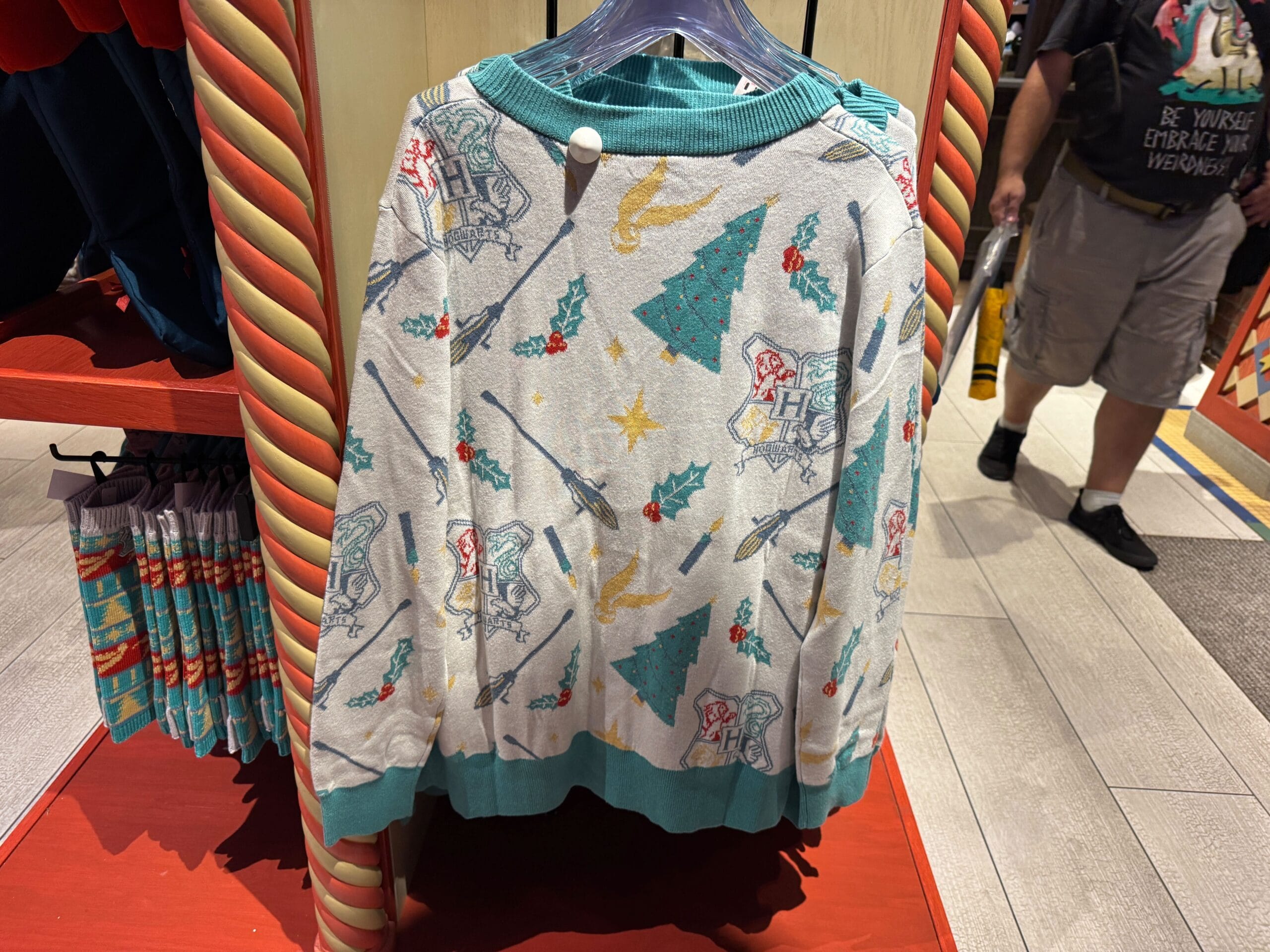 A sweater decorated with Hogwarts crests, broomsticks, and stars—perfect Harry Potter Christmas merch on display in store.