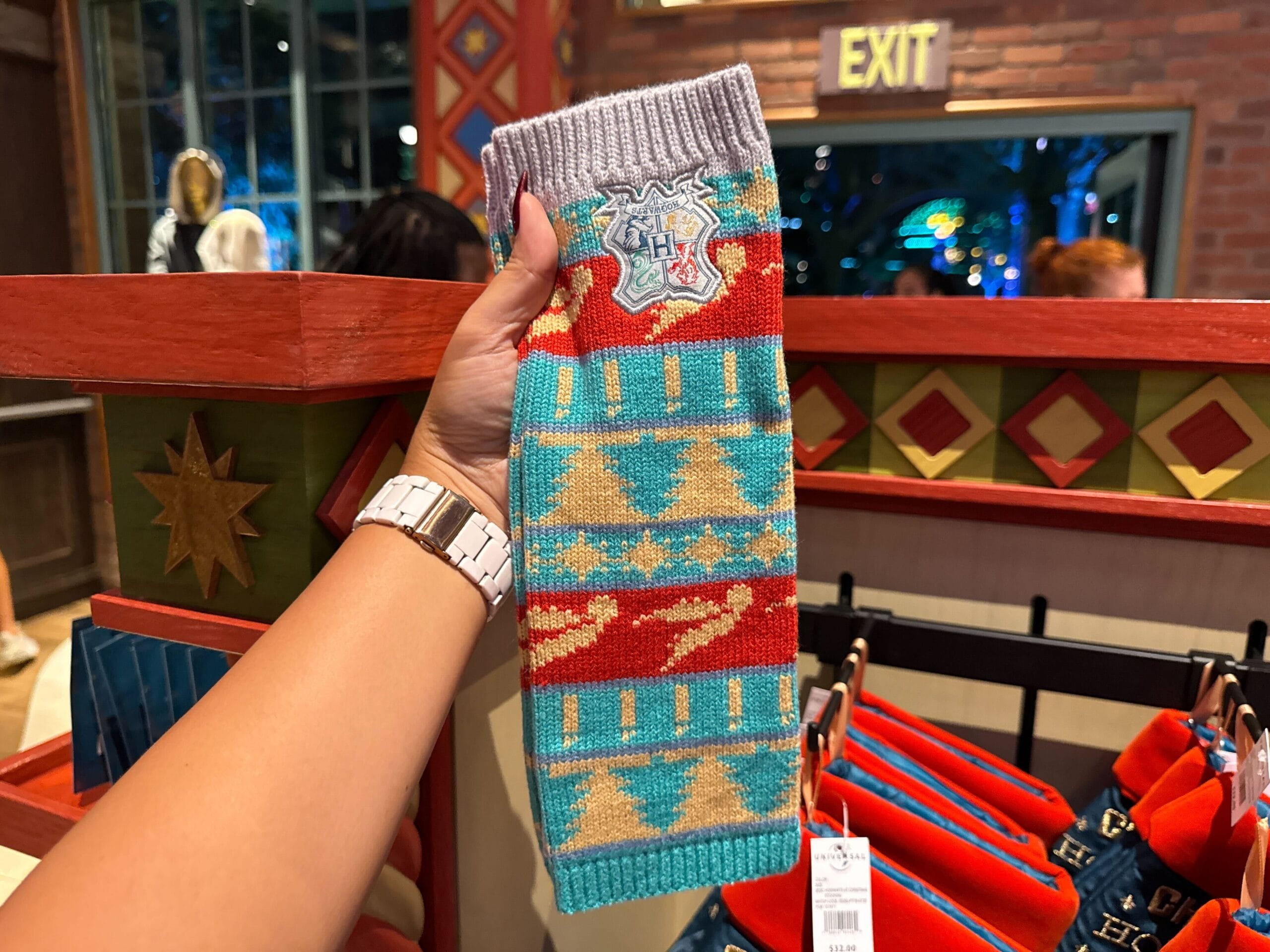 A hand holds a colorful knit Hogwarts scarf, perfect Harry Potter Christmas merch, in a festive store display.