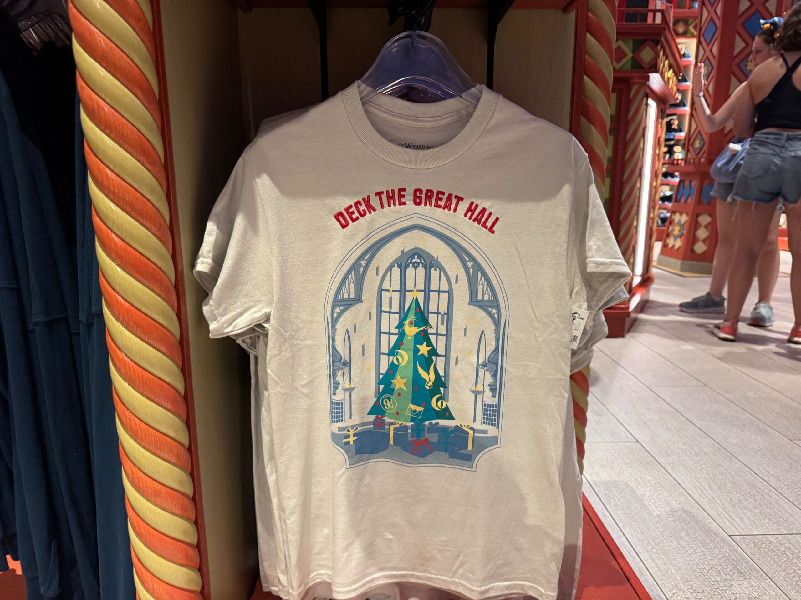 White t-shirt with "Deck the Great Hall" text and a Christmas at Hogwarts tree in a grand, arched windowed hall.