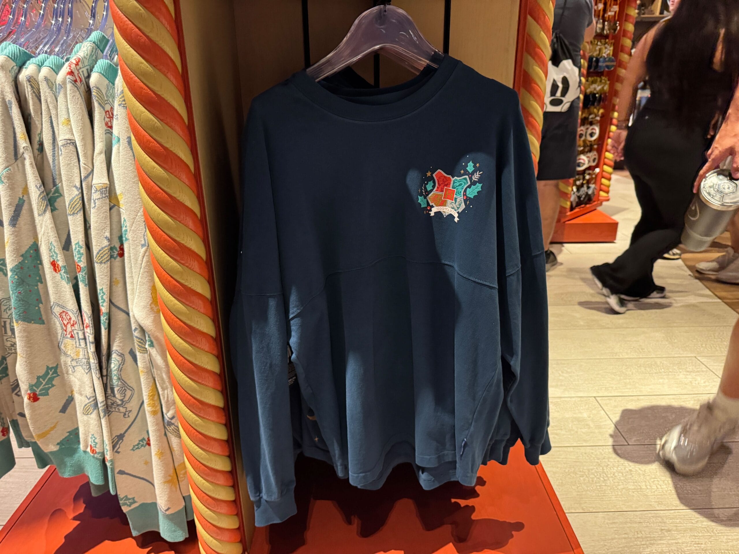 Navy blue sweatshirt with a small Harry Potter Christmas graphic on the chest, hanging on a rack in a store.