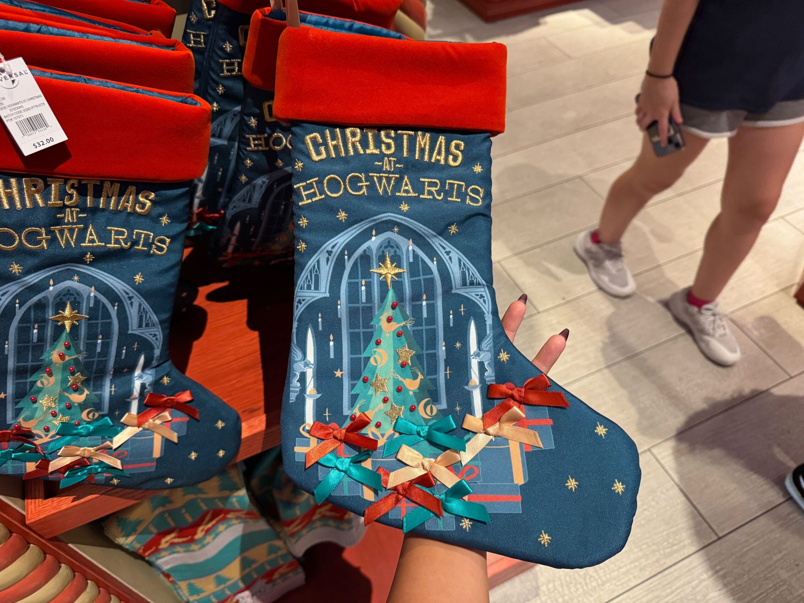 A hand holds a "Christmas at Hogwarts" stocking—perfect Hogwarts merch for a magical Harry Potter Christmas.