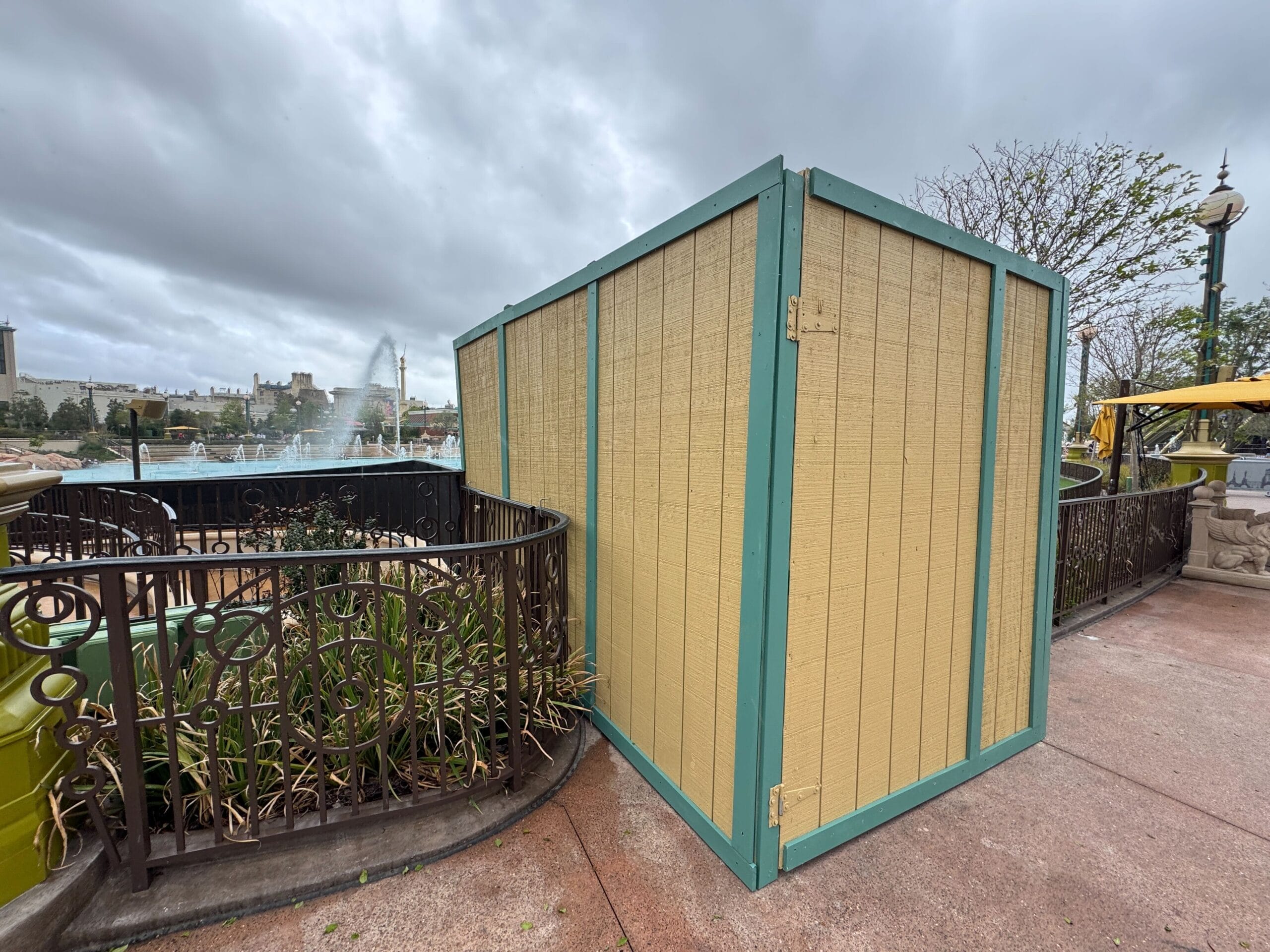 A tan construction wall blocks access near the Mario Fountain and ornate railing under a cloudy sky.