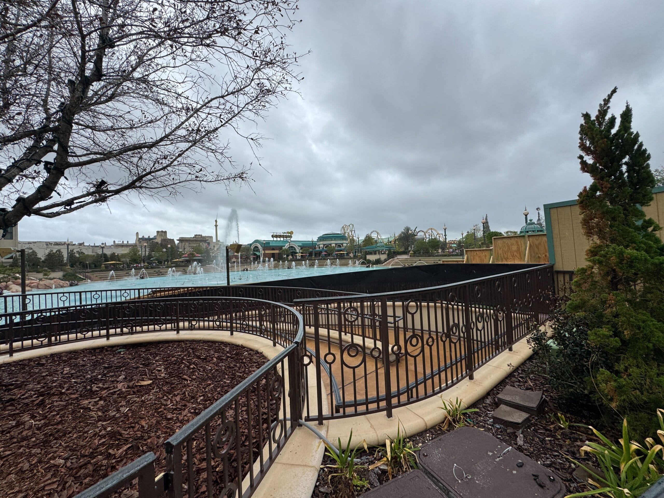 Overcast day at Epic Universe theme park, with railings, bare trees, and water features near the Mario Fountain.