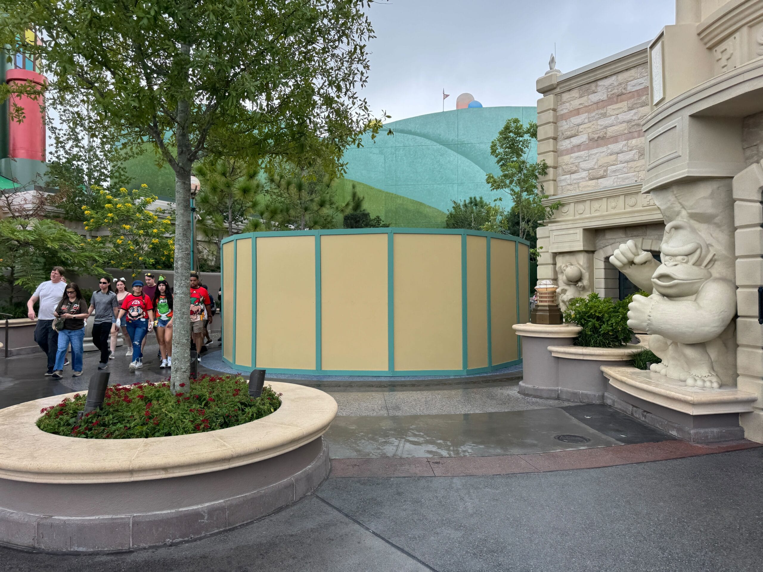 A beige construction wall at Epic Universe, with people passing by and a white Mario Fountain statue on the right.