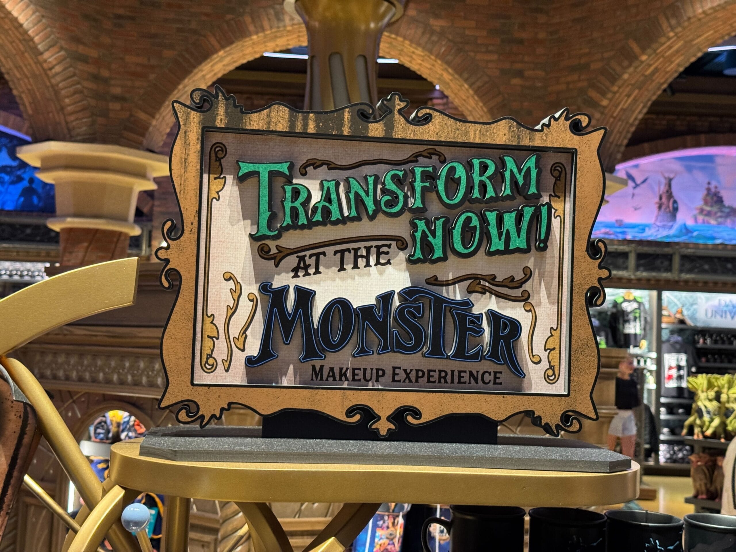 Epic Universe signage advertising "Transform Now! At the Monster Makeup Experience" in a themed, decorative shop setting.