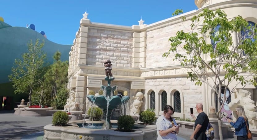 People stand near the Mario Fountain and cartoon statues at Epic Universe on a sunny day.