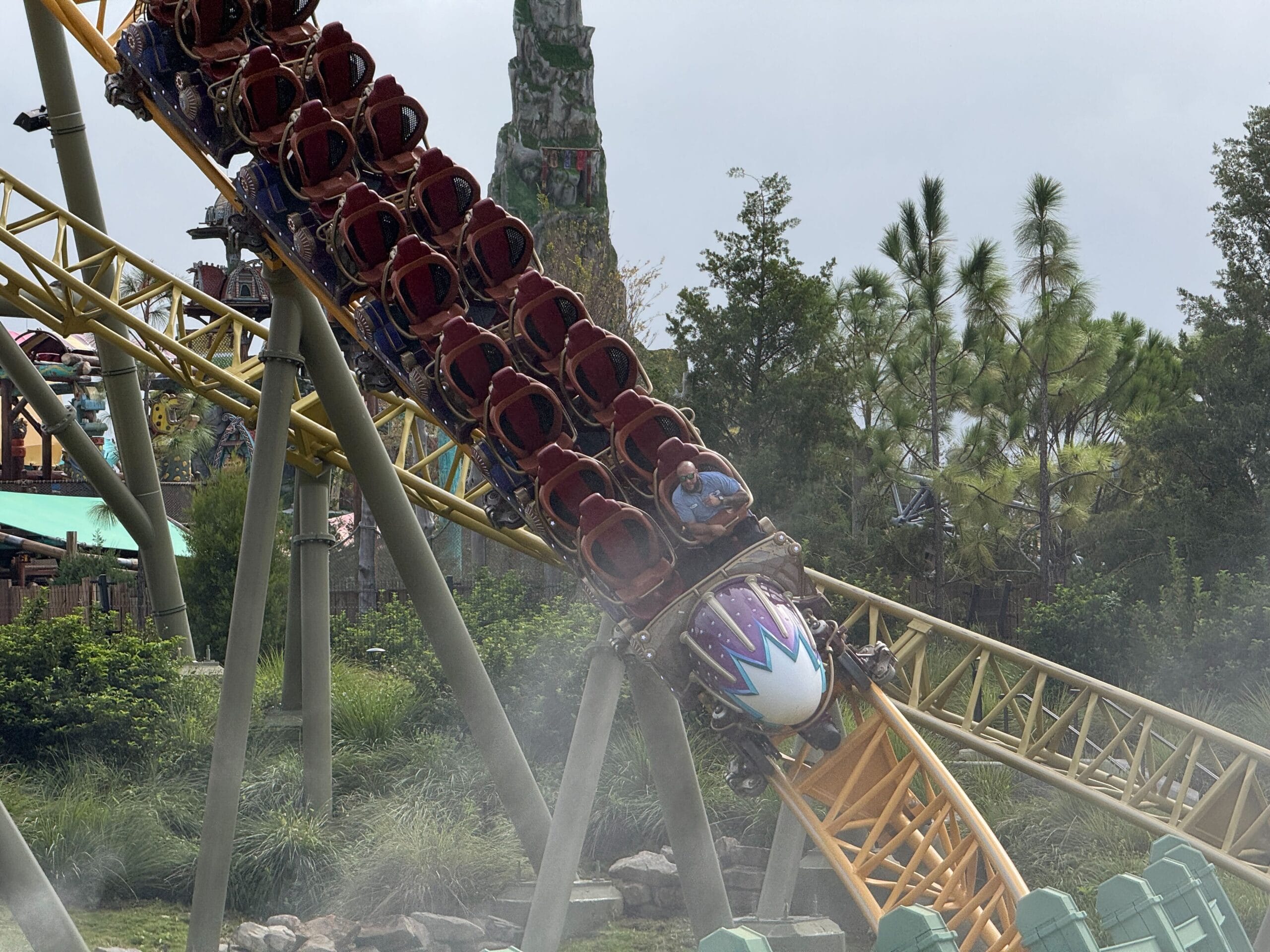 The Stardust Racers train with empty seats speeds down a yellow track, testing before reopening amid greenery and mist.