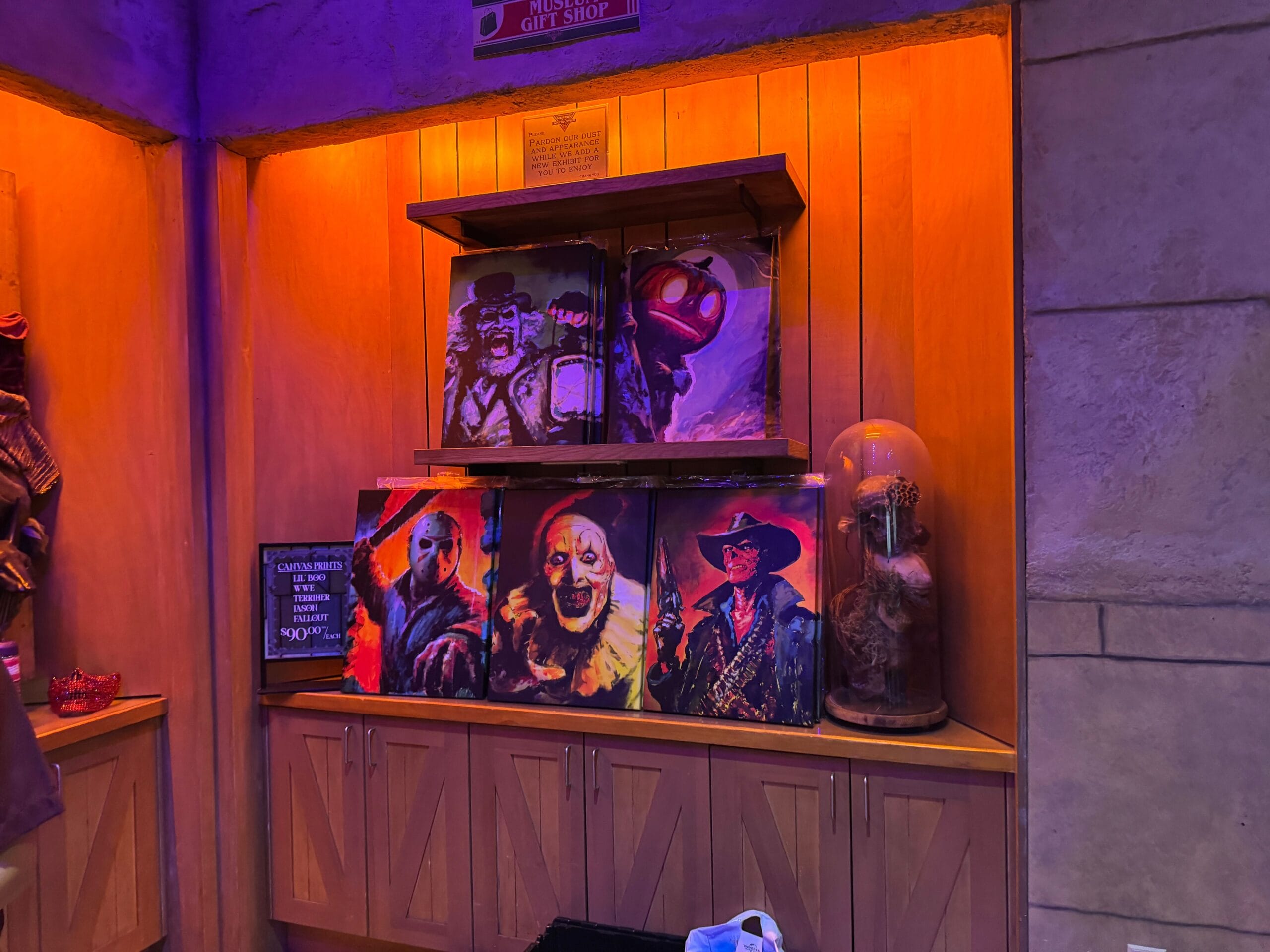Canvas prints of Halloween Horror Nights characters, including Lil' Boo, Jason, Art the Clown, and the Ghoul from Fallout, on a display.