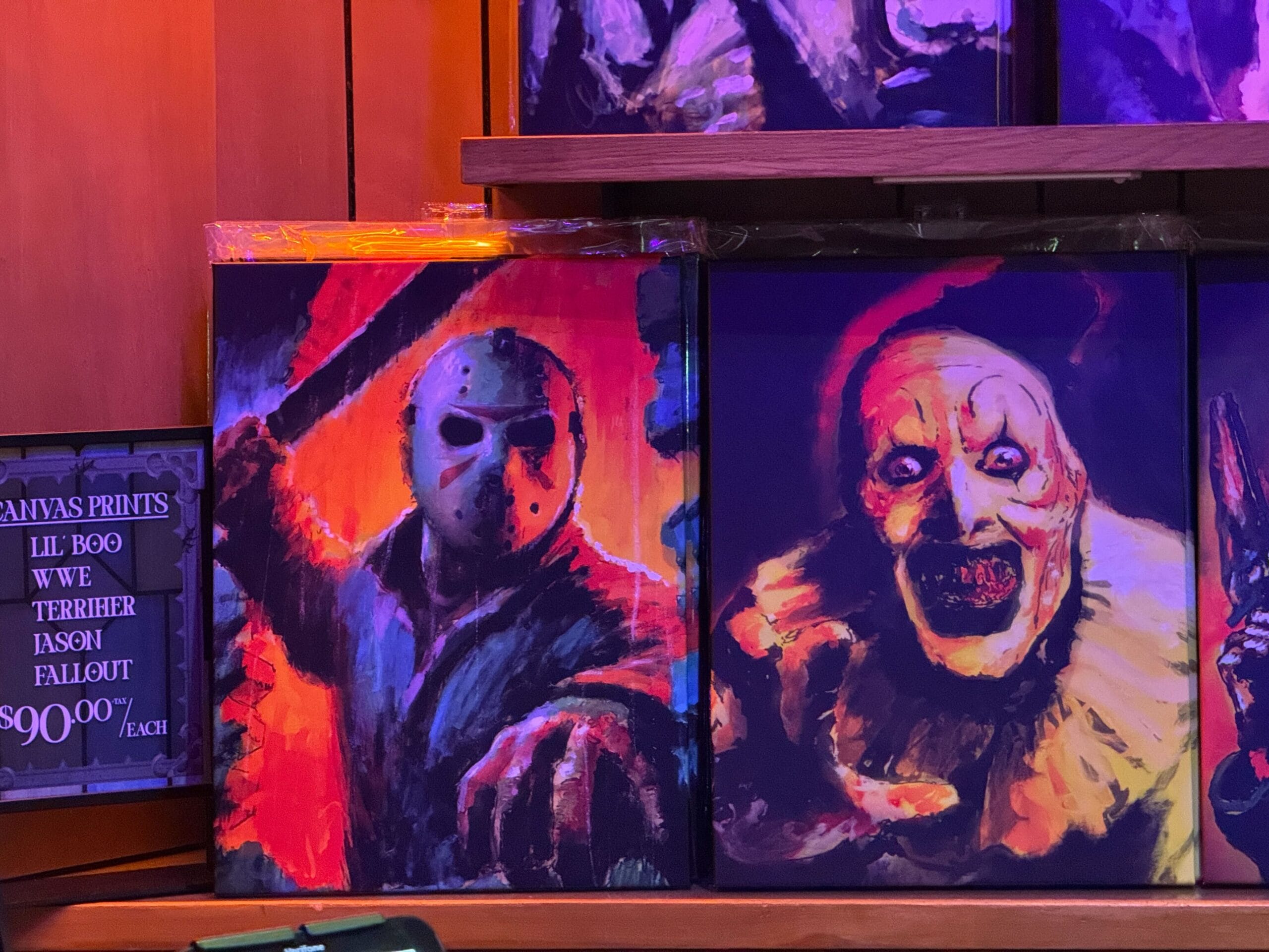 Colorful canvas prints of masked characters, including Jason, sit on a wooden shelf—unlike any artwork seen at Disney parks.