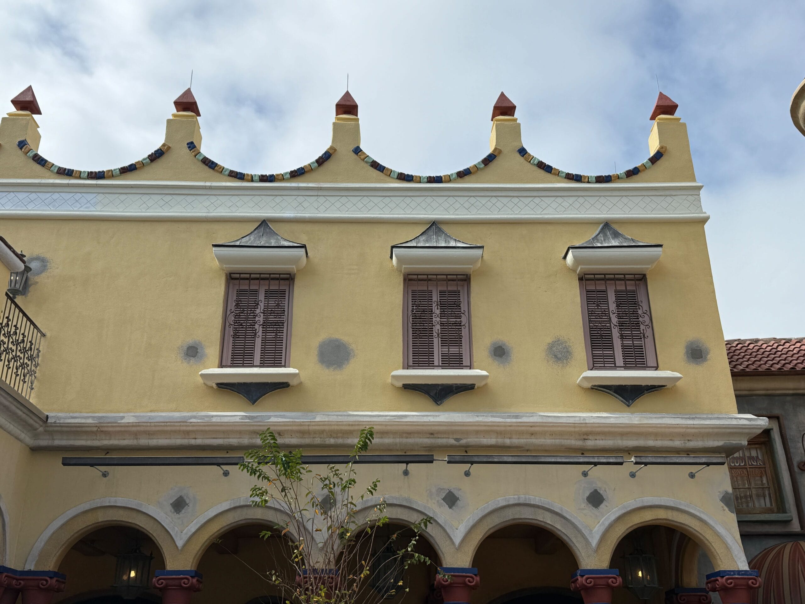 Yellow building with three shuttered windows, arched doorways, and ornate trim—reminiscent of architecture found in Disney parks.