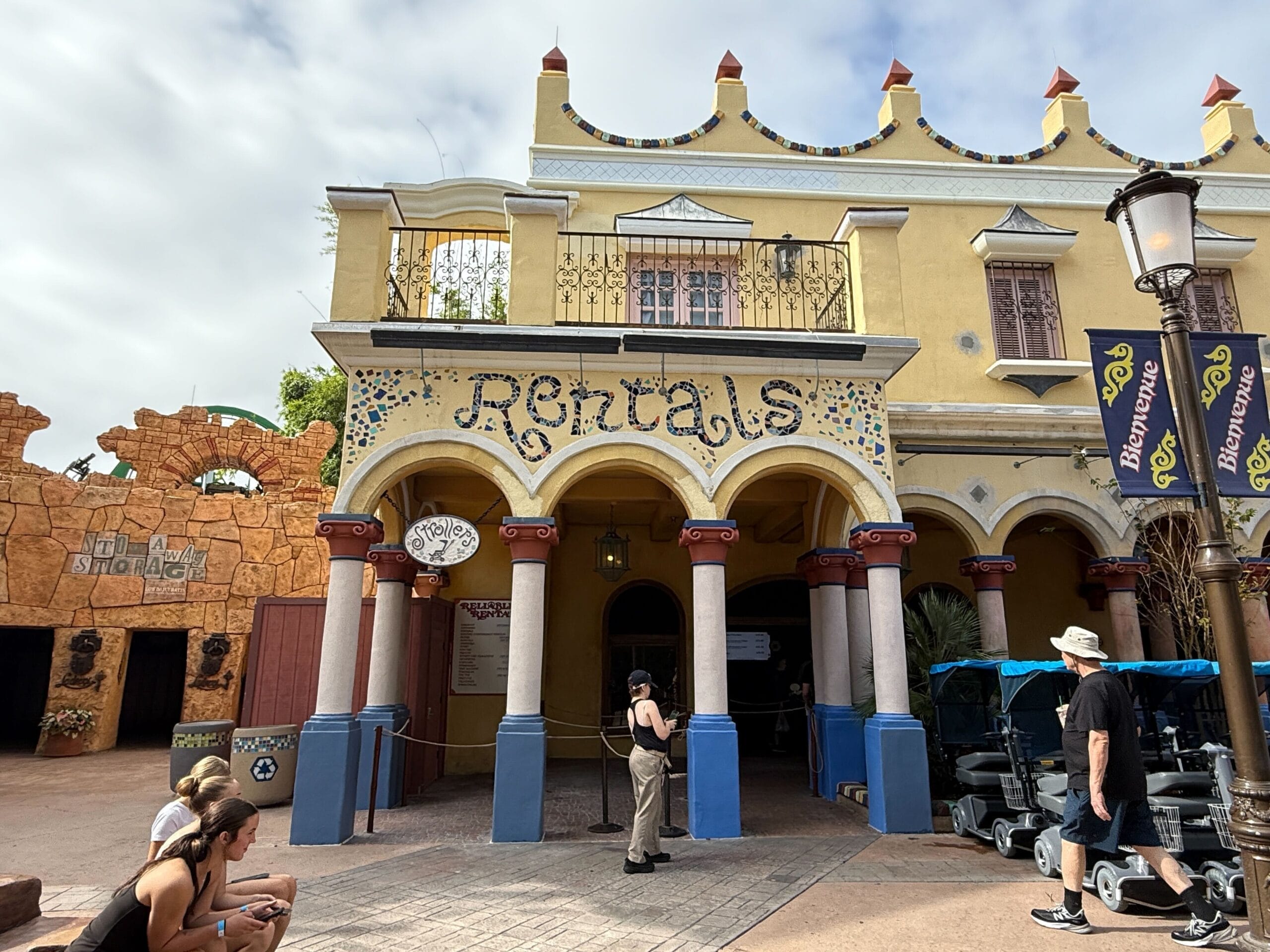 Yellow and tan building with arched columns, a "Rentals" sign, and strollers outside, like those near Disney park entrances.