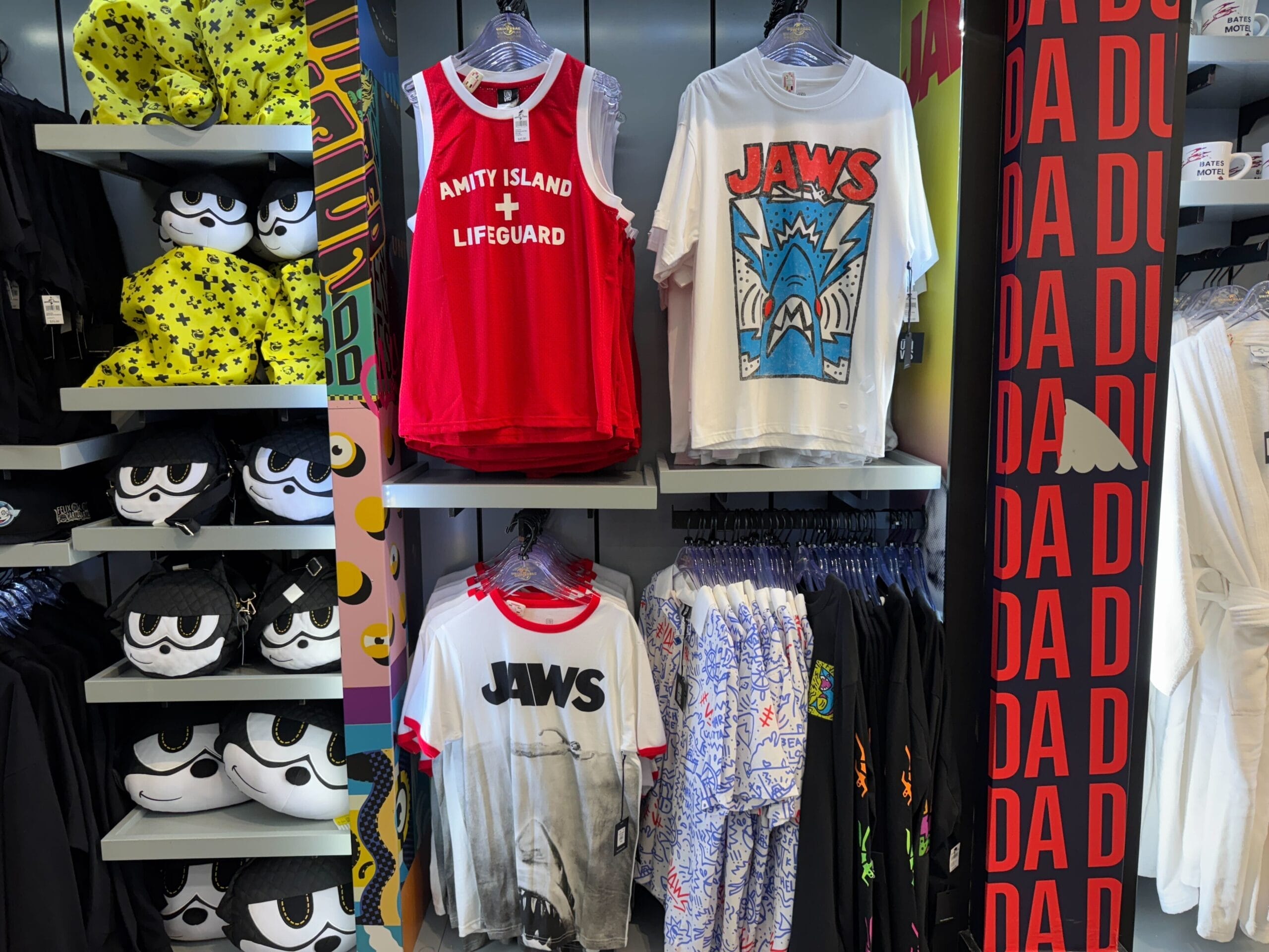 A Jaws-themed store display featuring shirts and plush toys in front of a "DA DA" red wall, not part of any Disney park.