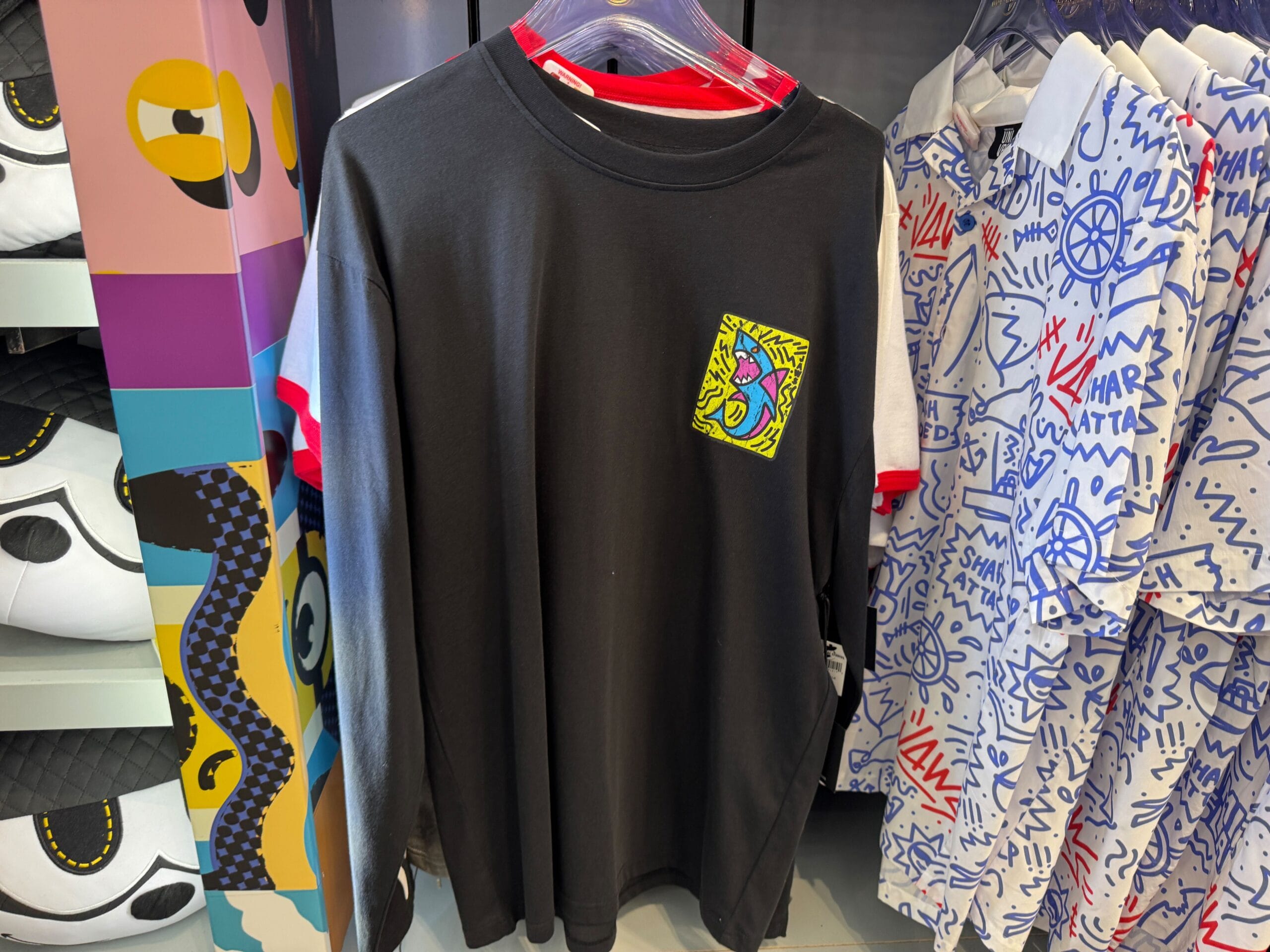 Black long-sleeve shirt with bright abstract face patch, surrounded by lively patterned shirts, like bold styles seen at Disney parks.