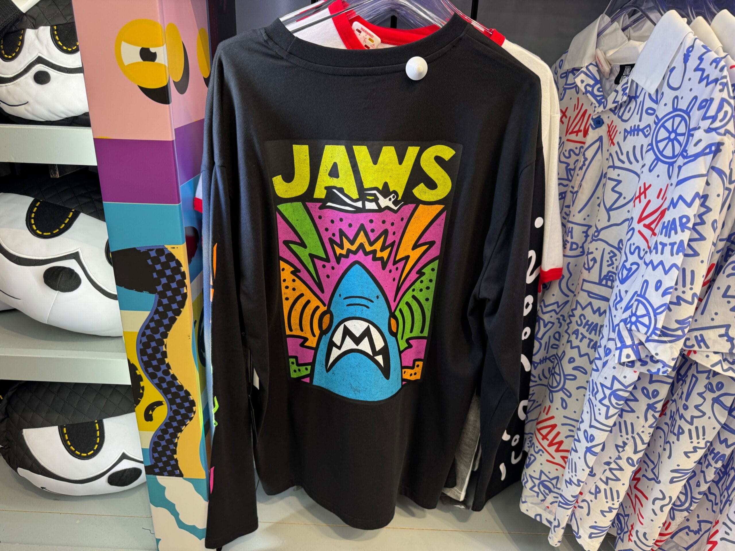 Black long-sleeve shirt with a vibrant, cartoon-style "JAWS" shark graphic, similar to fun attire found at Disney parks stores.