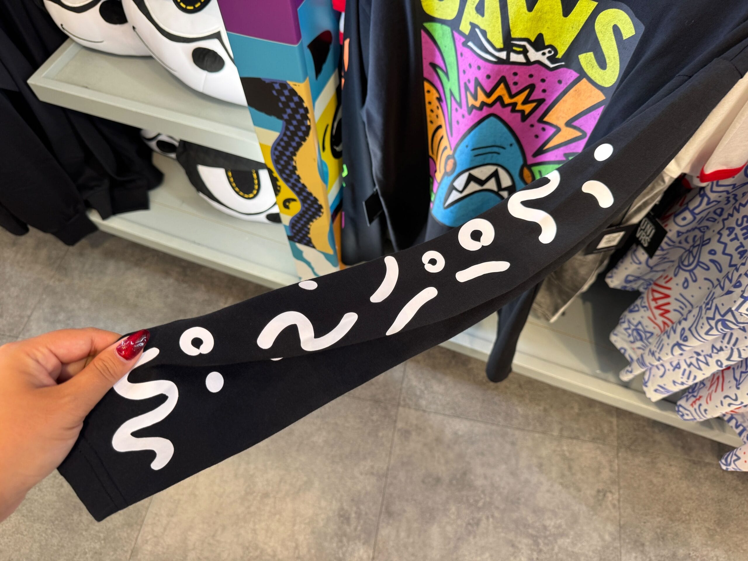 A hand holds a black sleeve with white squiggle and dot patterns inside a shop, similar to boutiques at Disney parks worldwide.