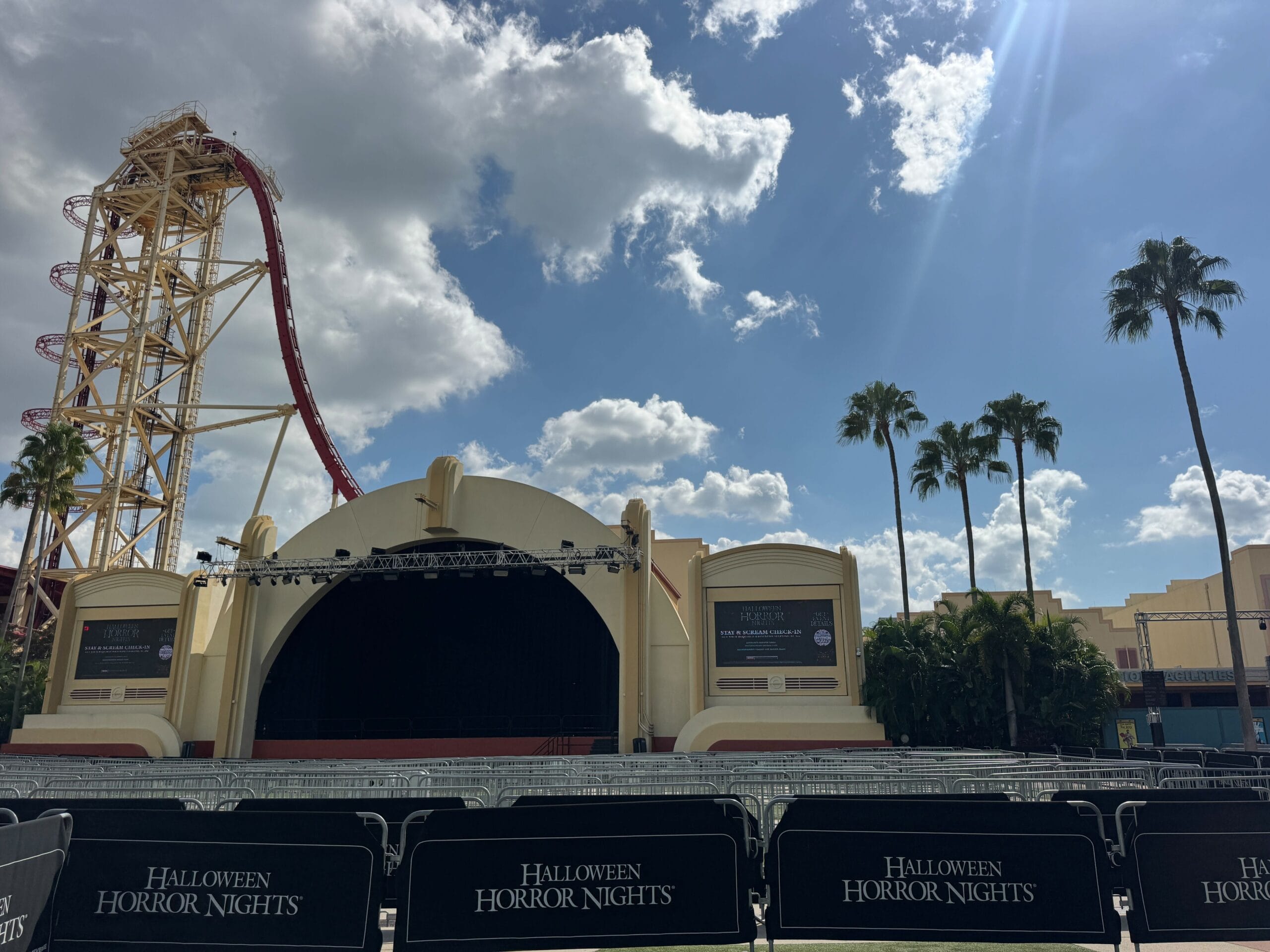 Outdoor stage with “Halloween Horror Nights” barriers, Hollywood Rip Ride Rockit coaster, and palm trees at Universal Studios Florida.