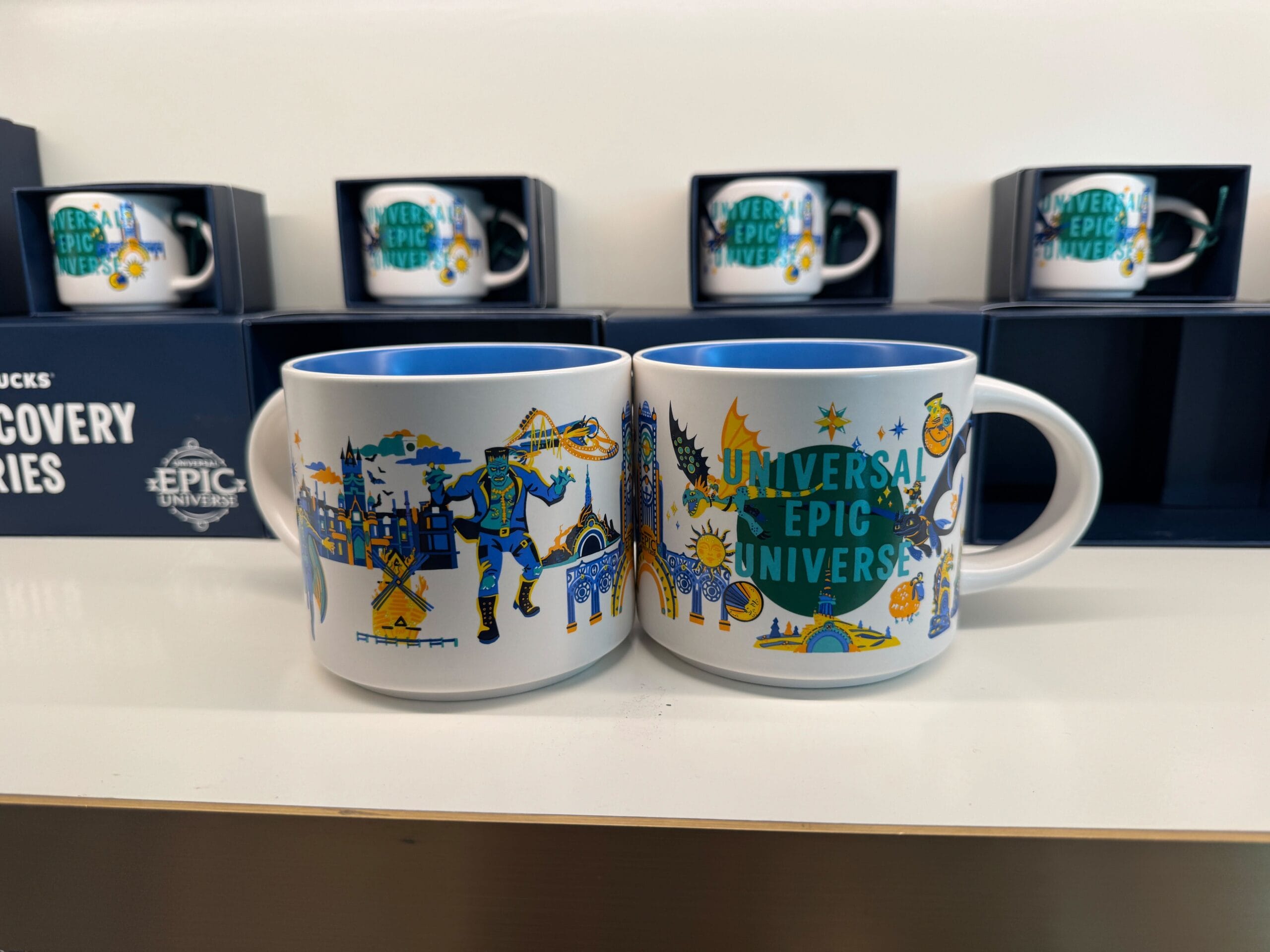Two vibrant Universal Epic Universe mugs with themed artwork on a white shelf—more bold than Disney souvenir mugs at castle shops.