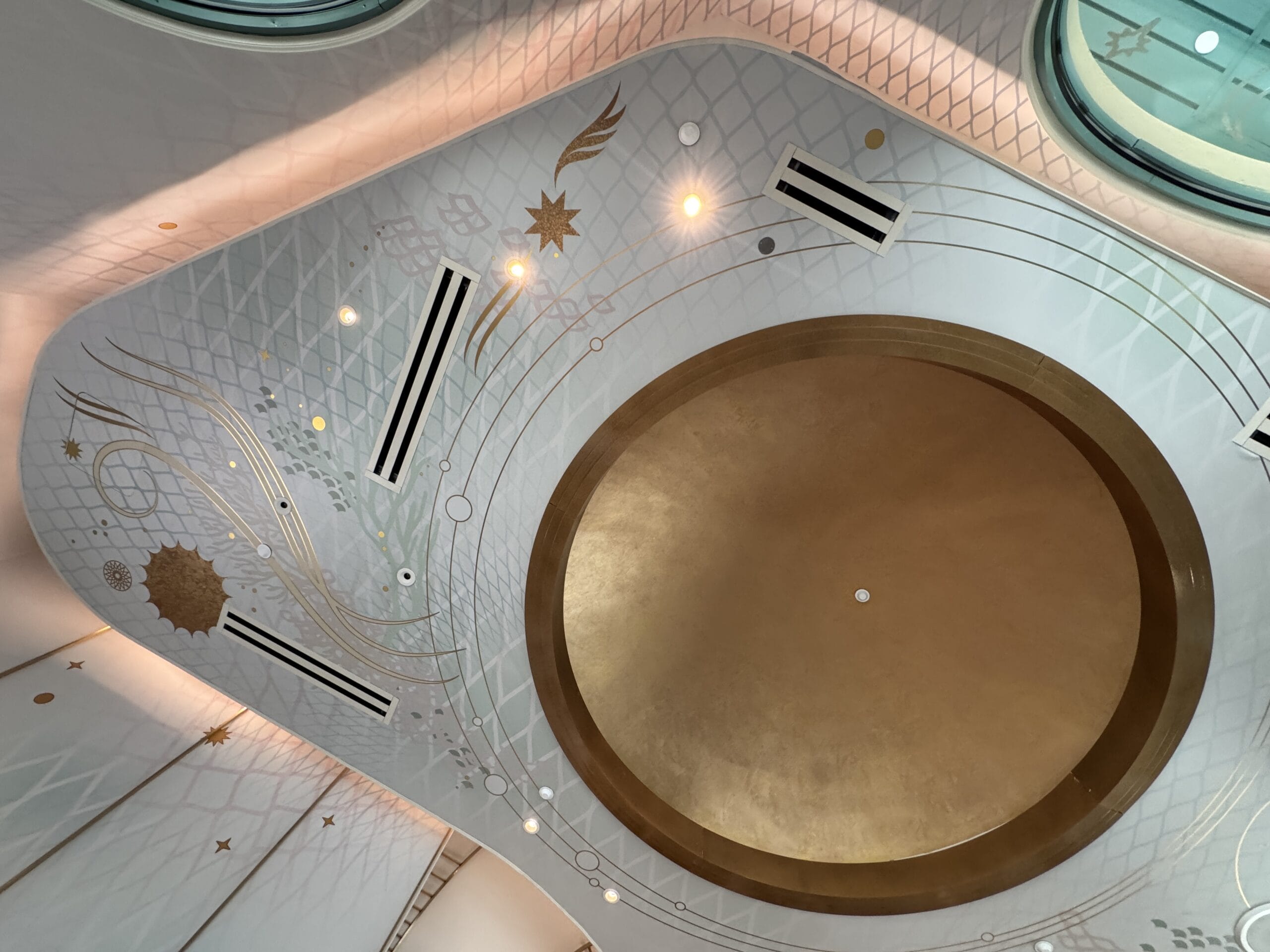 Ceiling with a large gold circular center, geometric details and gold accents, similar in grandeur to Disney castle interiors.