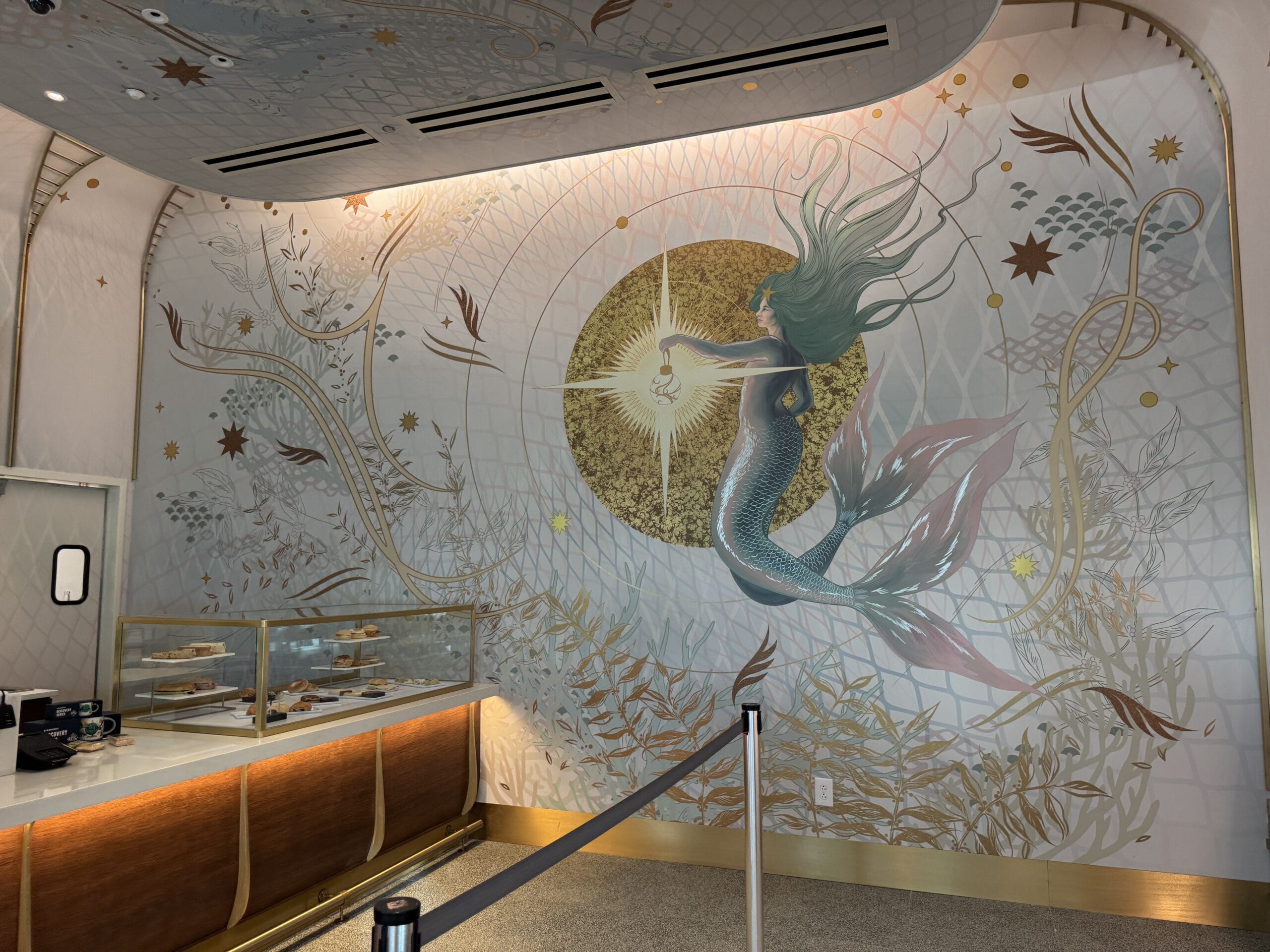 A mural at Epic Universe shows a mermaid with a glowing orb, surrounded by sea plants and Starbucks pastries—no Disney castle in view.