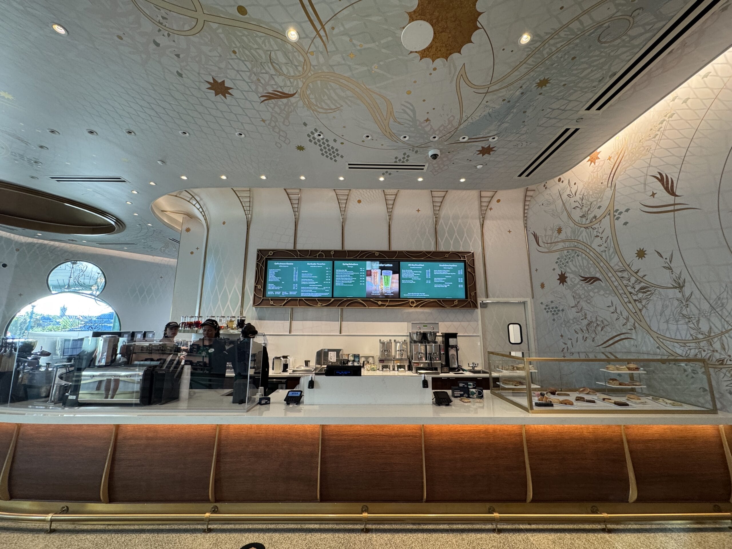 Modern café in a Disney park, featuring elegant white and gold accents, digital menus, and Starbucks treats reminiscent of Main Street.
