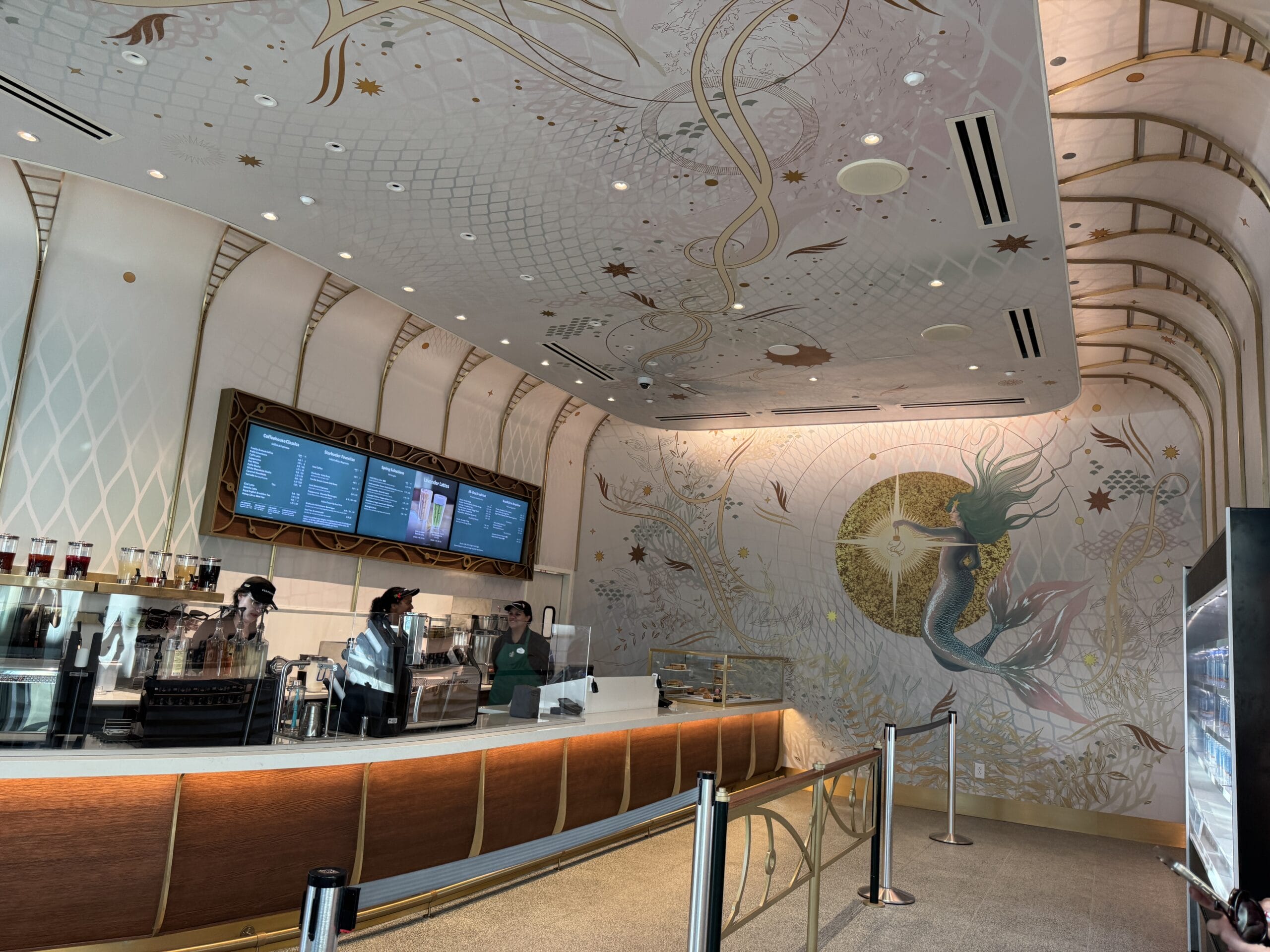 A sleek Starbucks with a mermaid mural, digital menus, and two baristas—not unlike Starbucks spots near Disney castles worldwide.